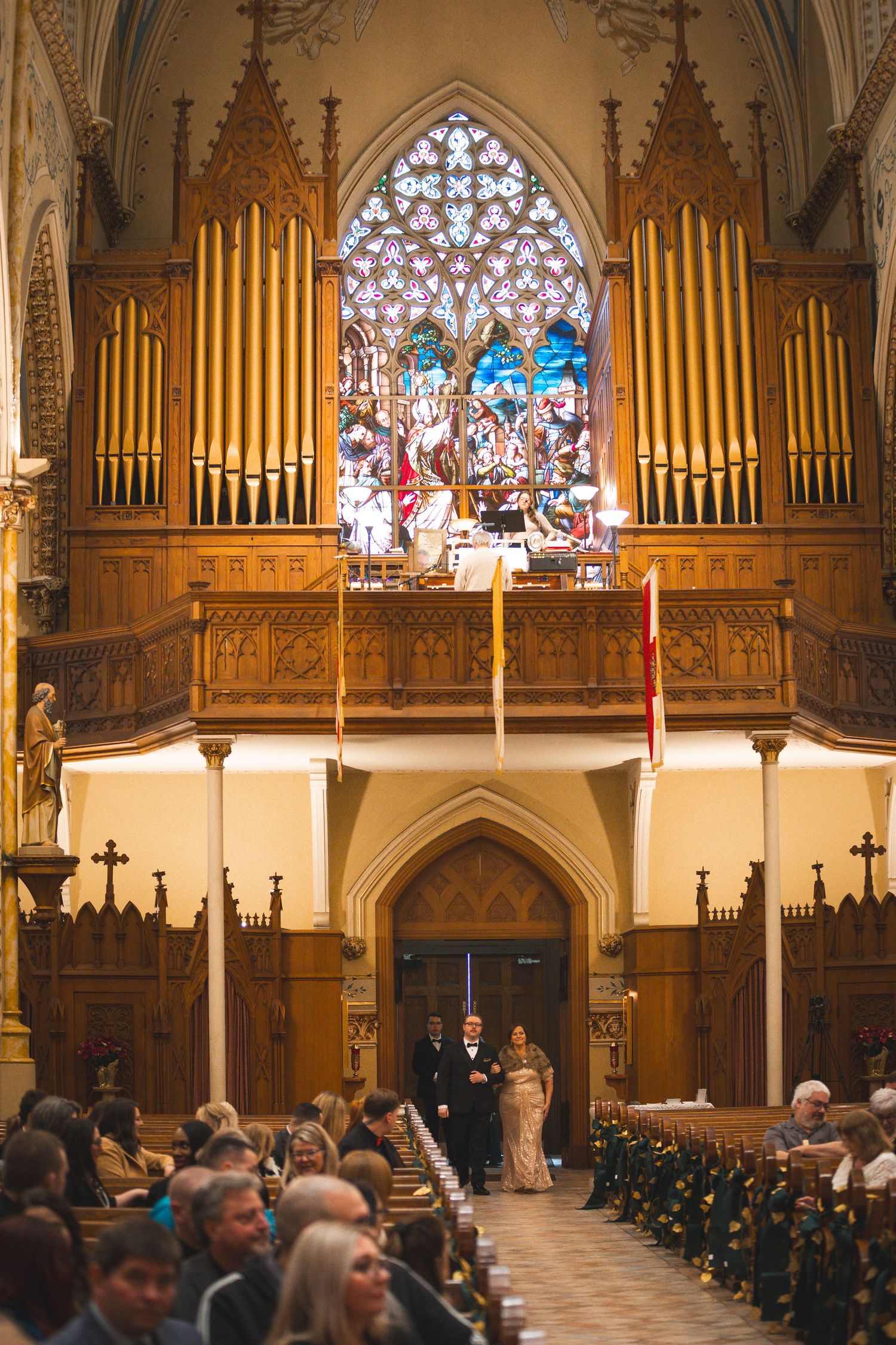 A traditional church wedding ceremony beneath towering organ pipes and stained glass windows.