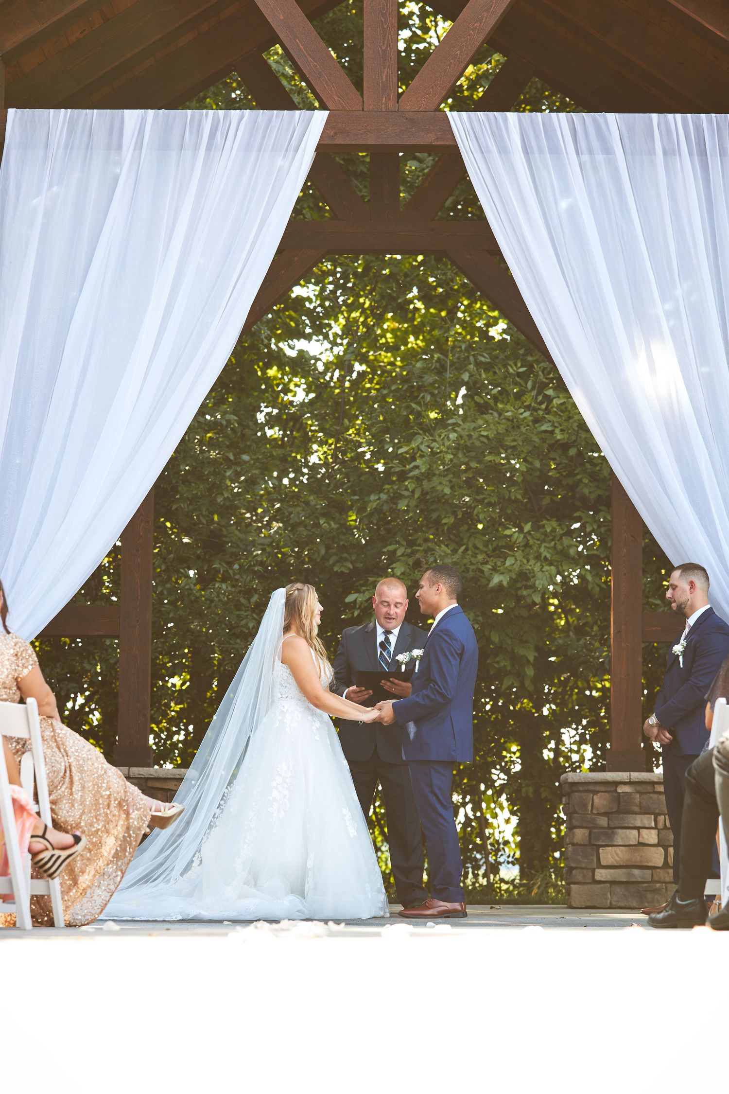An elegant outdoor wedding ceremony space with white drapes and wooden beams.