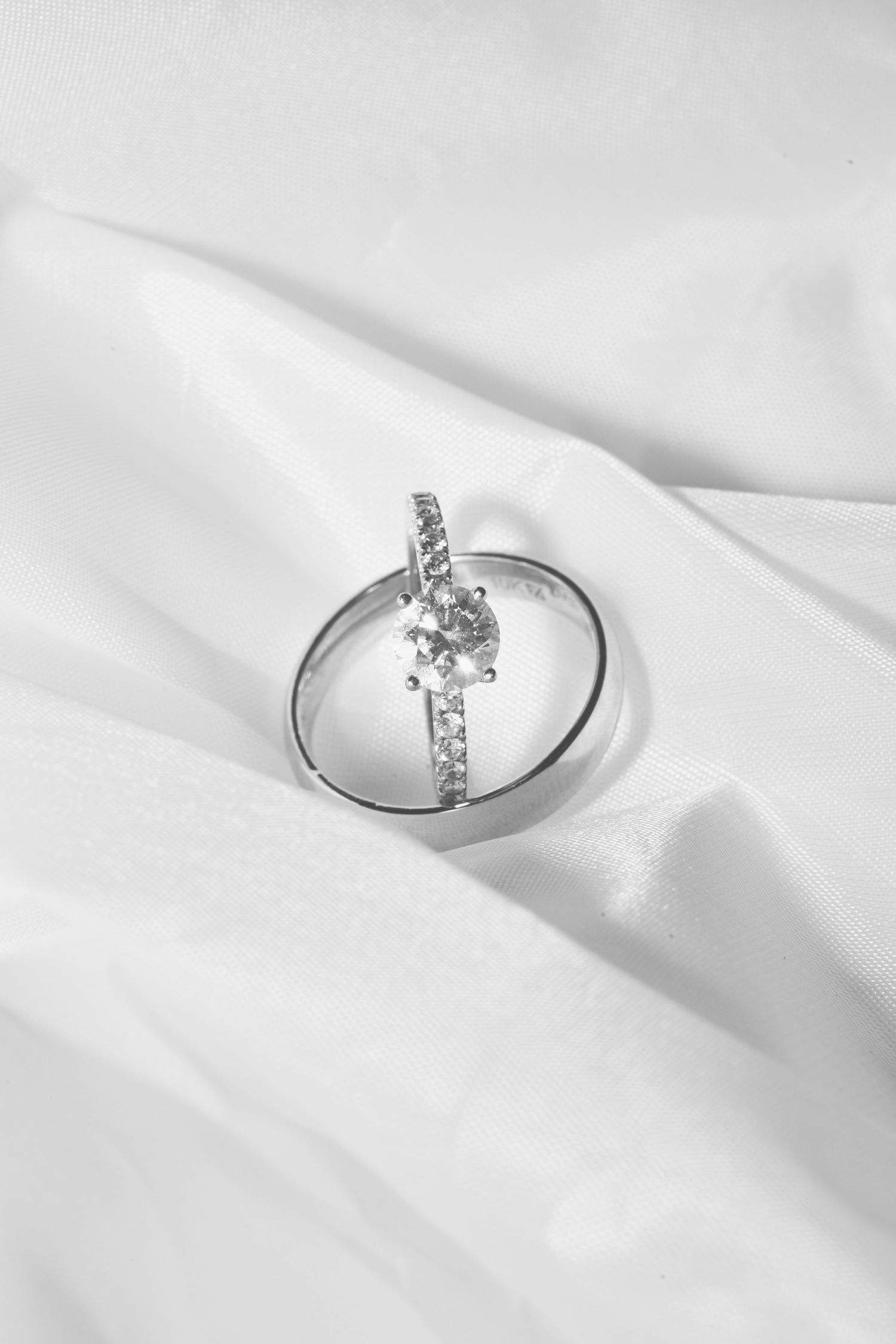 Minimalist diamond ring photographed on white silk fabric in natural light.