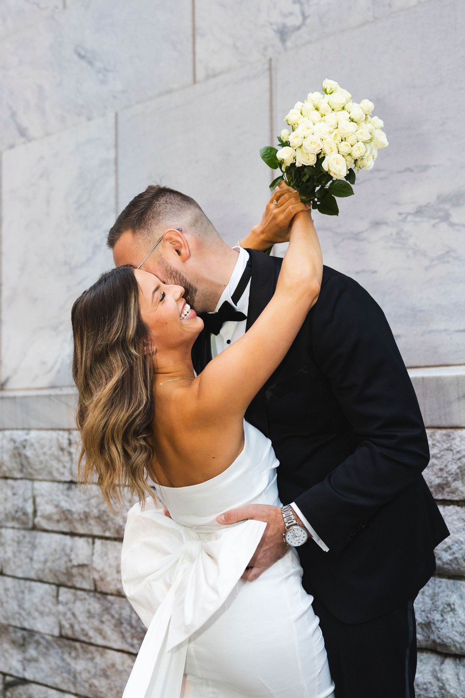 A tender wedding photoshoot moment captured against a marble wall backdrop.