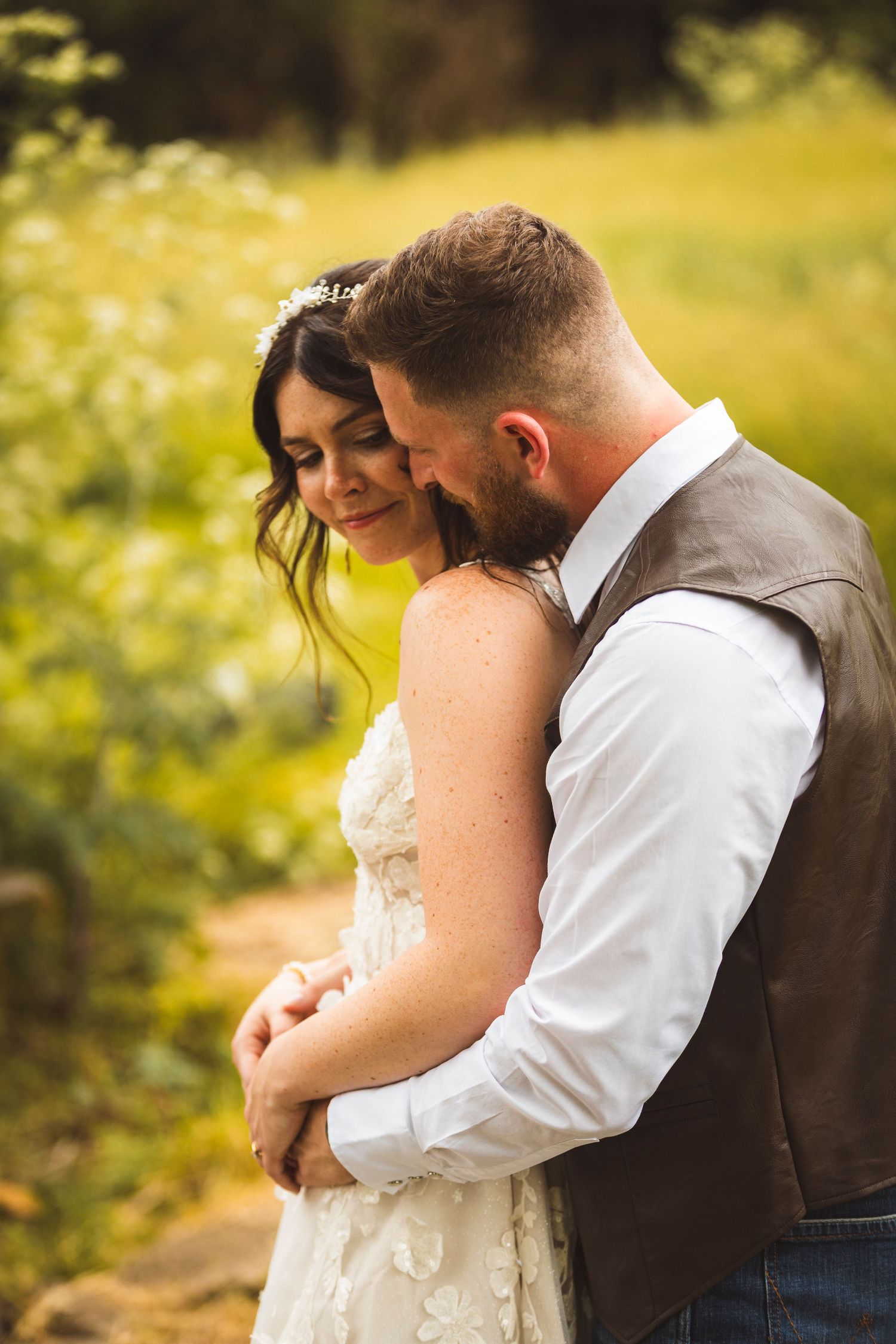 Intimate couple embraces in a sunlit meadow with golden wildflowers blooming around them.