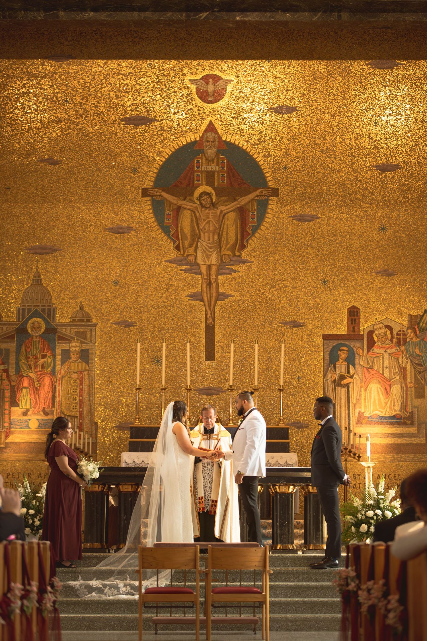 Religious wedding ceremony takes place in ornate church with golden mosaic walls and candles.