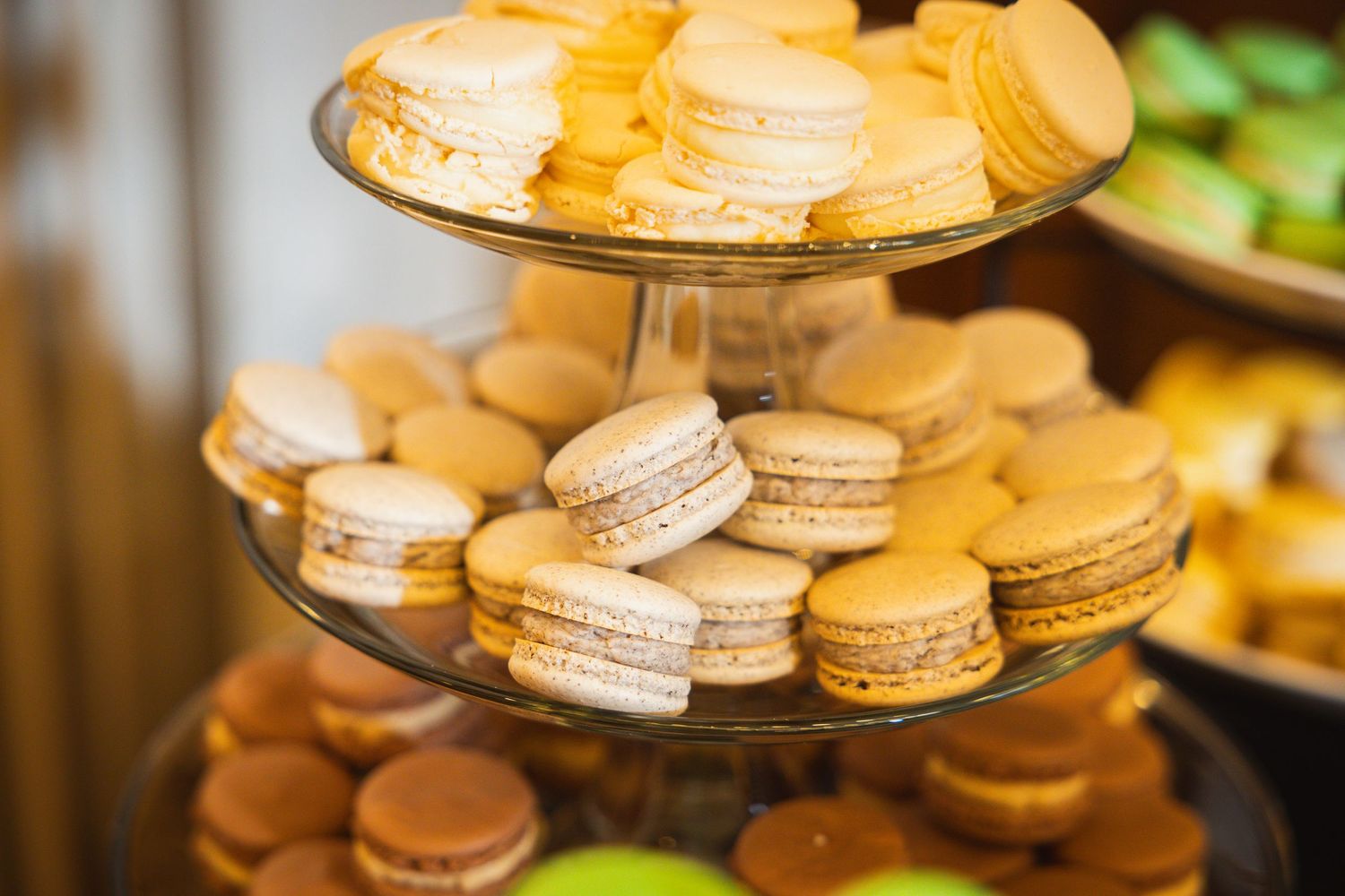 Elegant display of golden macarons and desserts arranged on tiered platters at a wedding reception.
