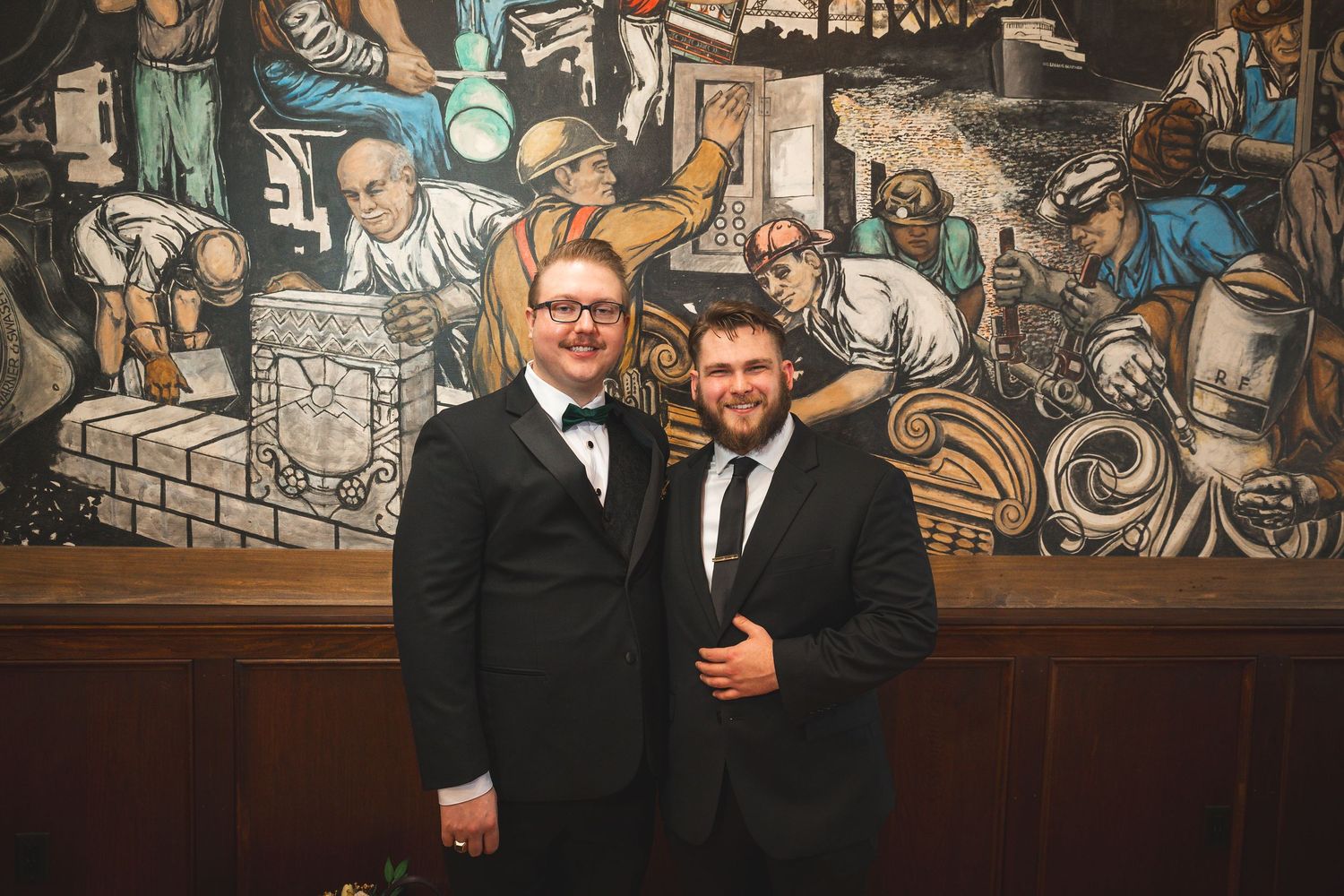 Wedding celebration group photo against vintage mural backdrop in historic venue setting.