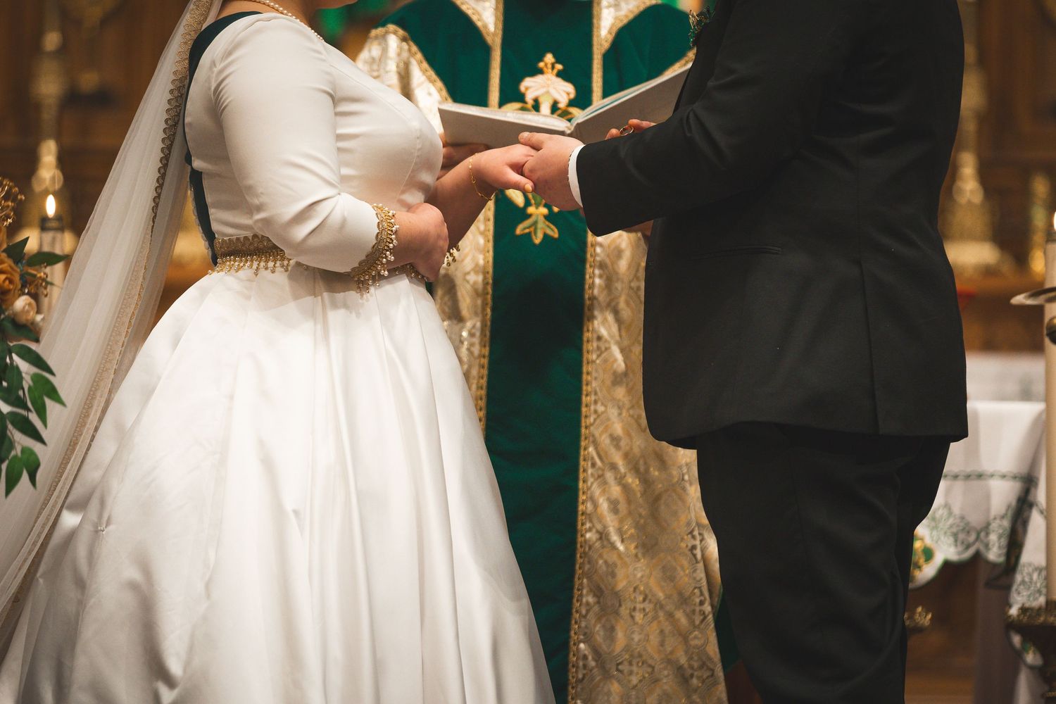 Wedding ceremony exchange of vows in front of elegant green and gold church altar.