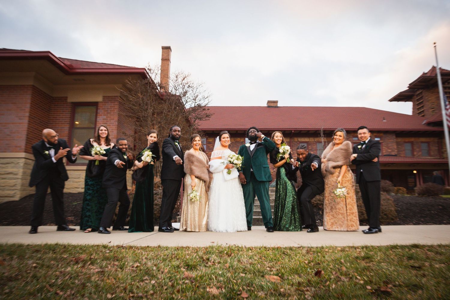 Wedding party lined up for photos outside historic building under cloudy skies.