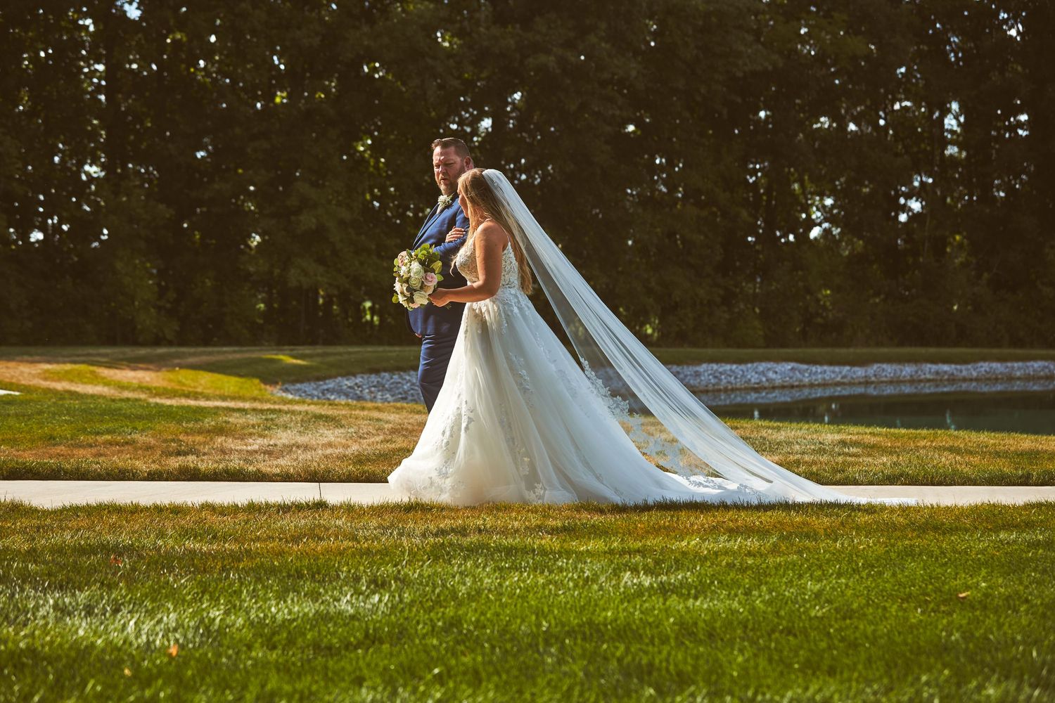 A couple in wedding attire poses on a grassy lawn at sunset.