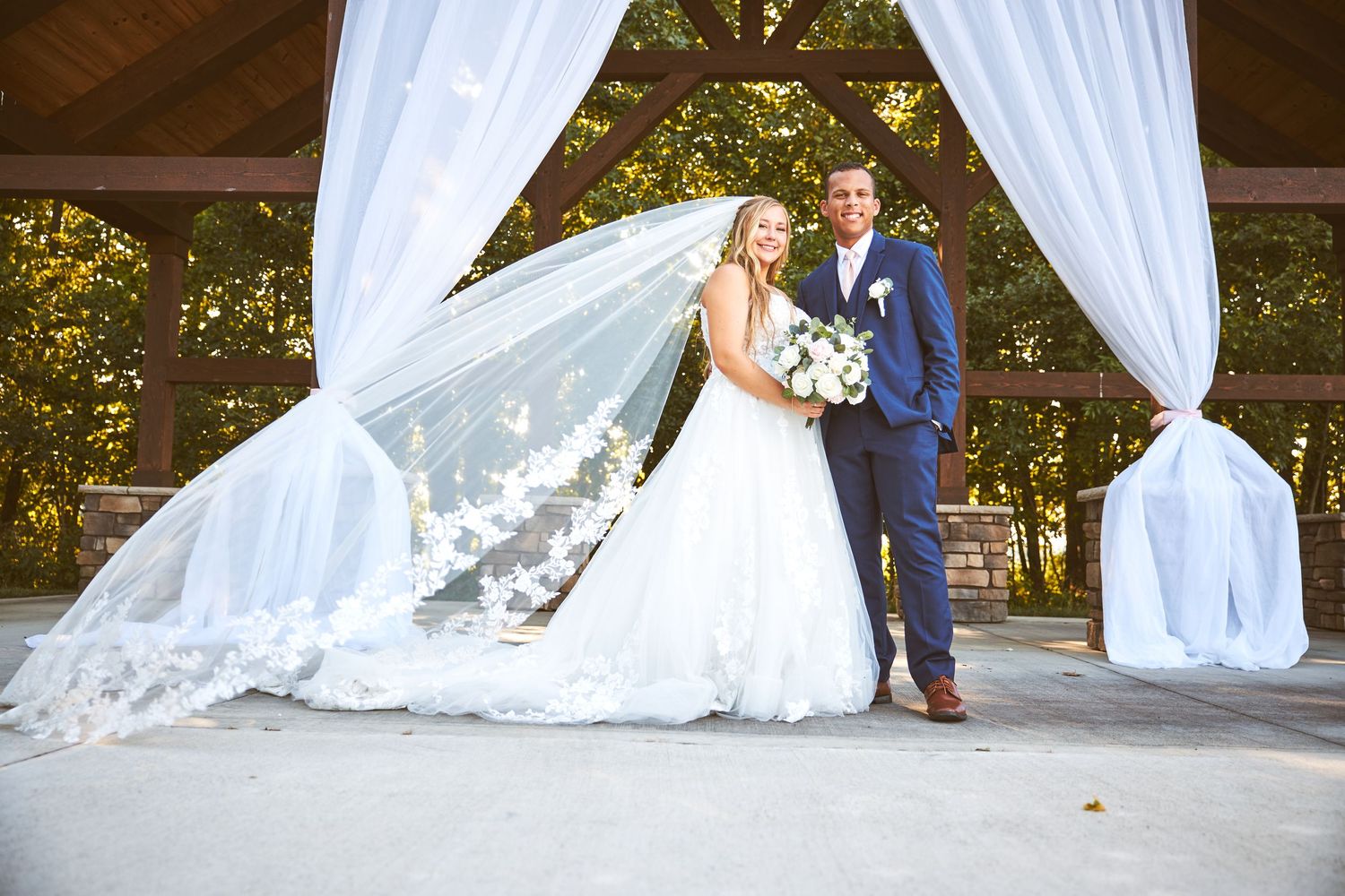 Scenic outdoor wedding ceremony setup with flowing white drapes and natural woodland backdrop.