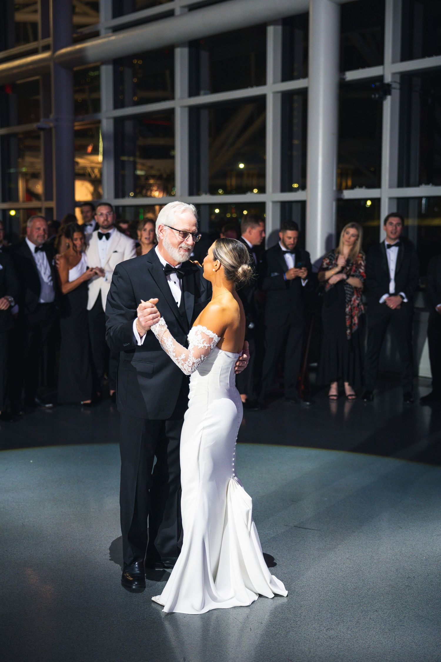 A couple shares an elegant dance moment during a formal wedding reception with guests watching.
