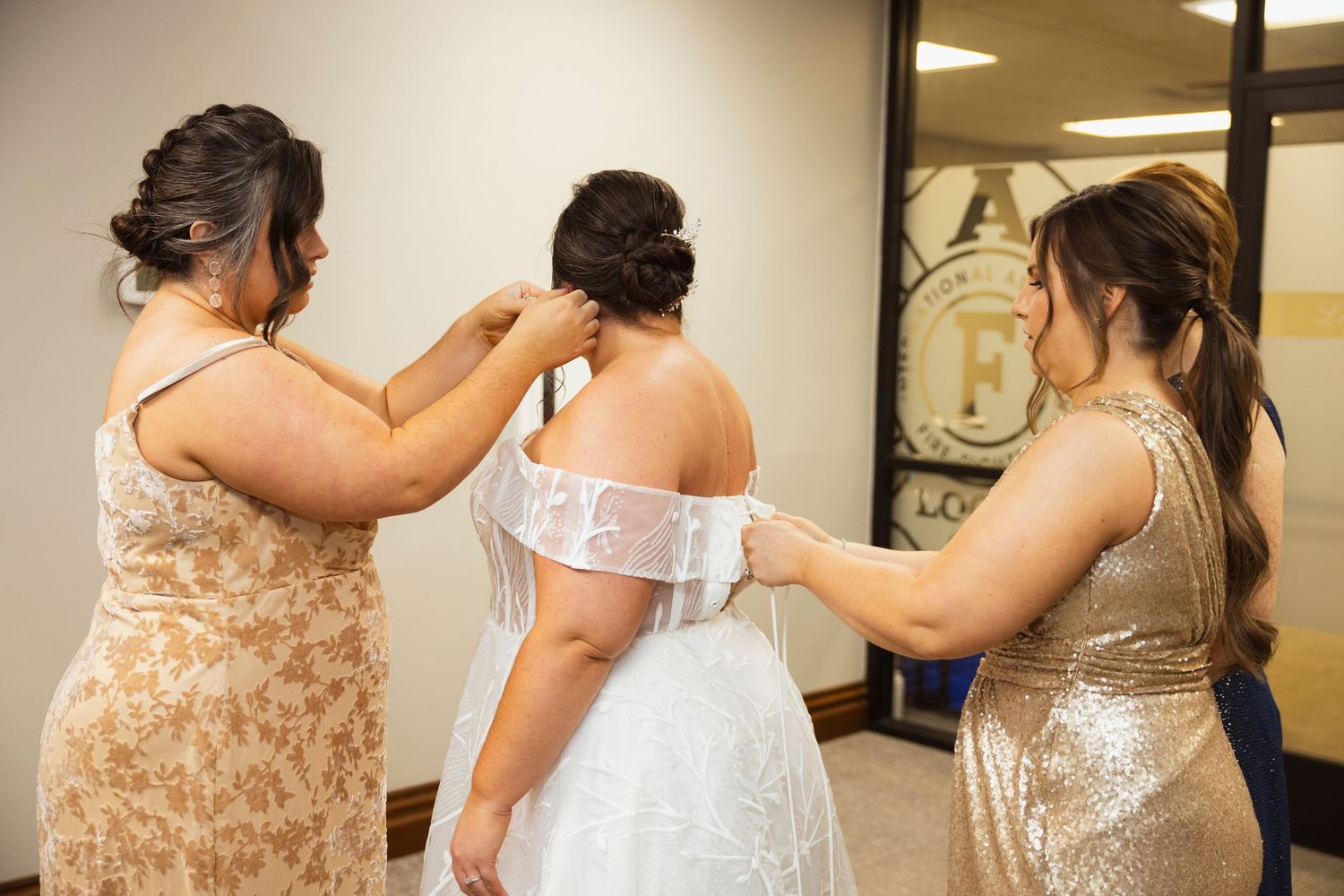Bridesmaids helping with final dress preparations in a dressing room.