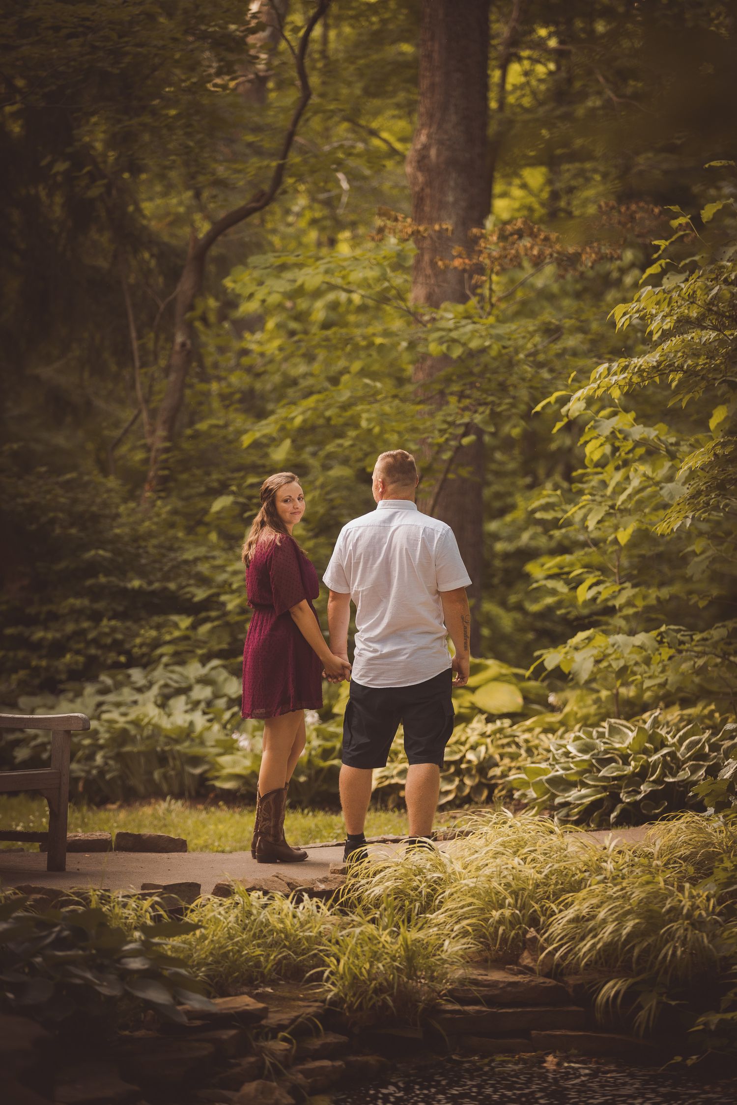 Couple walking along a wooded path surrounded by lush green foliage.
