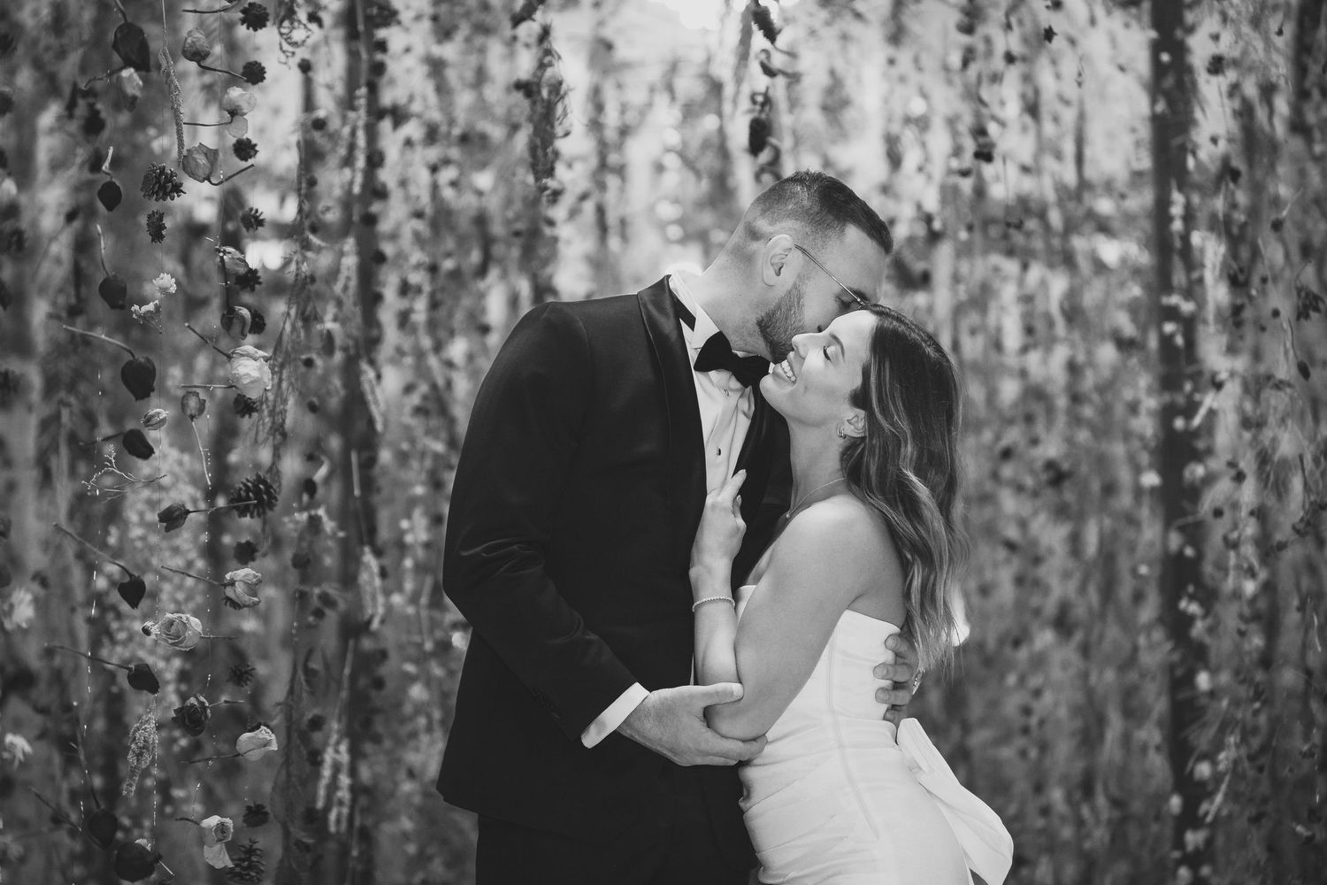 Wedding couple embracing under an enchanting canopy of hanging floral decorations.