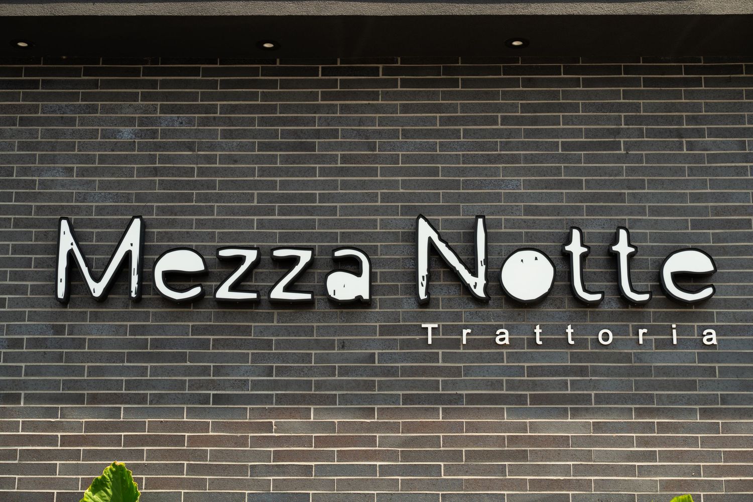 Modern storefront displaying 'Mezza Notte Trattoria' signage on dark brick exterior.
