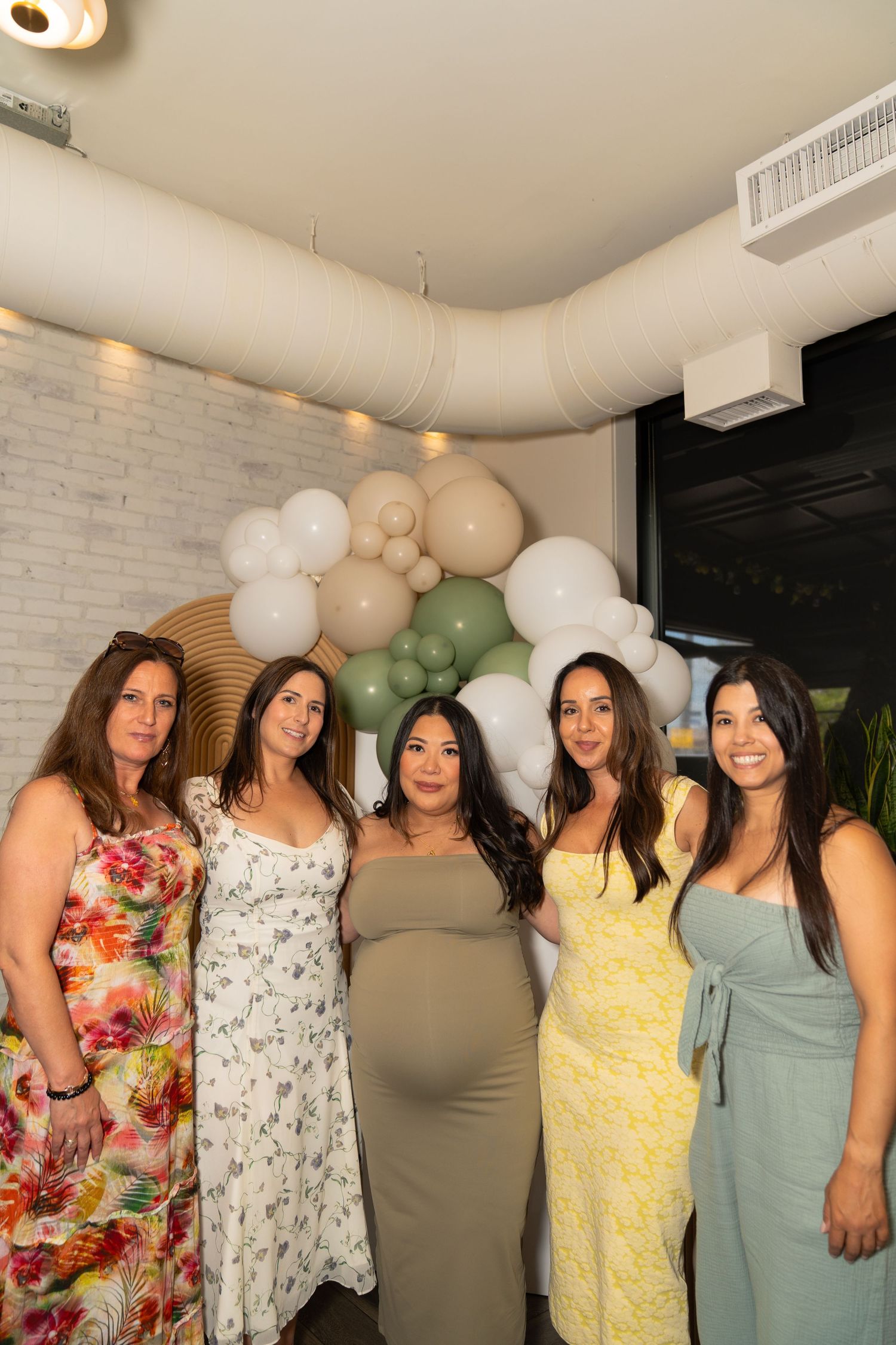 Celebration gathering with people in colorful summer dresses under balloon decorations.