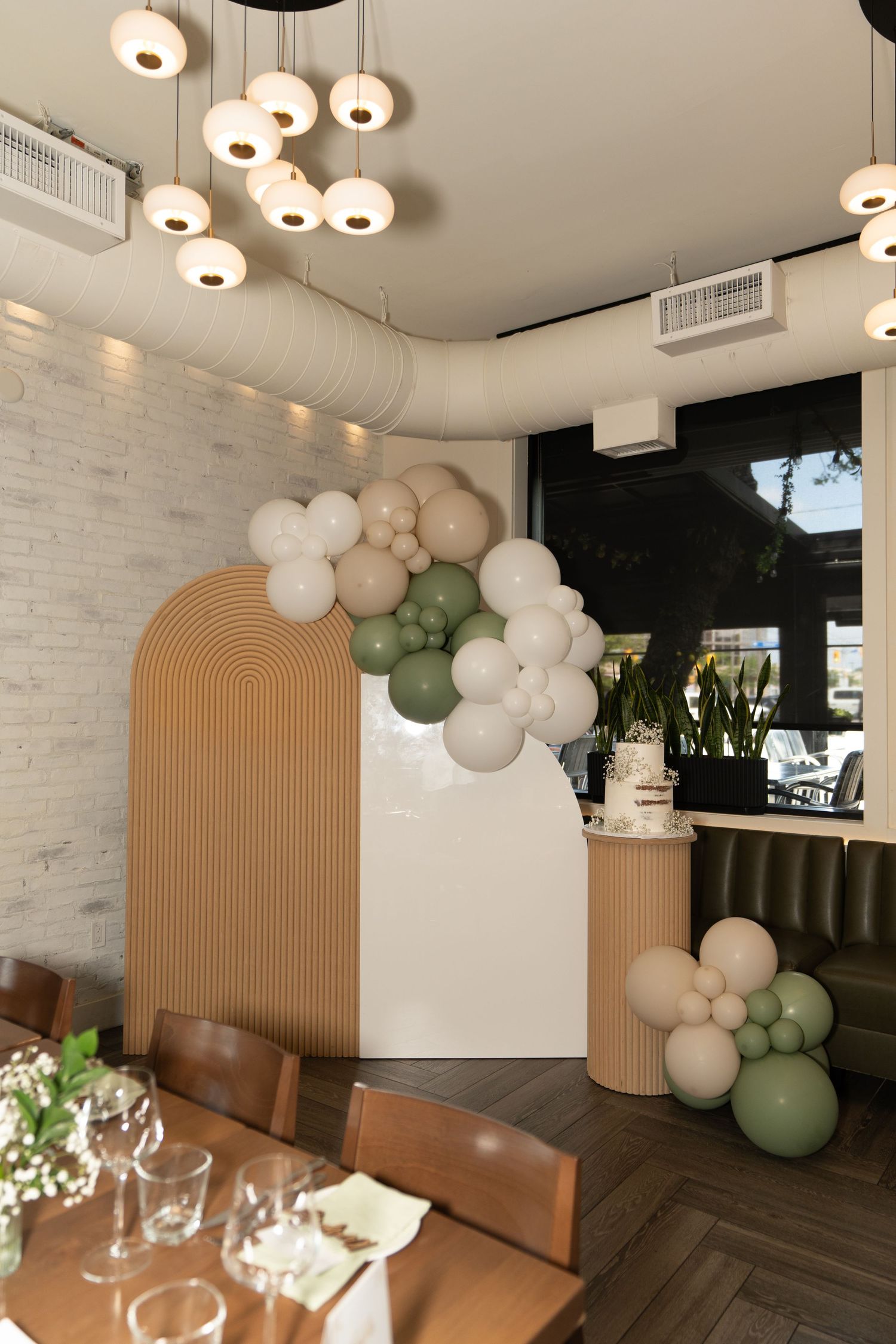 Modern restaurant interior with arched decor and balloon installations in white and sage green.