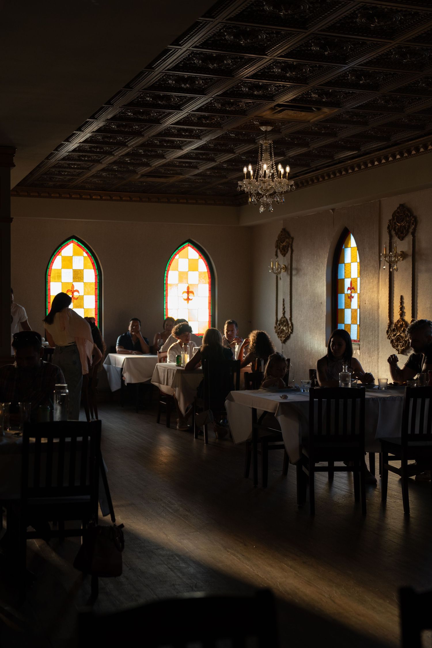 Gothic-style dining room with stained glass windows and chandelier creating dramatic lighting.
