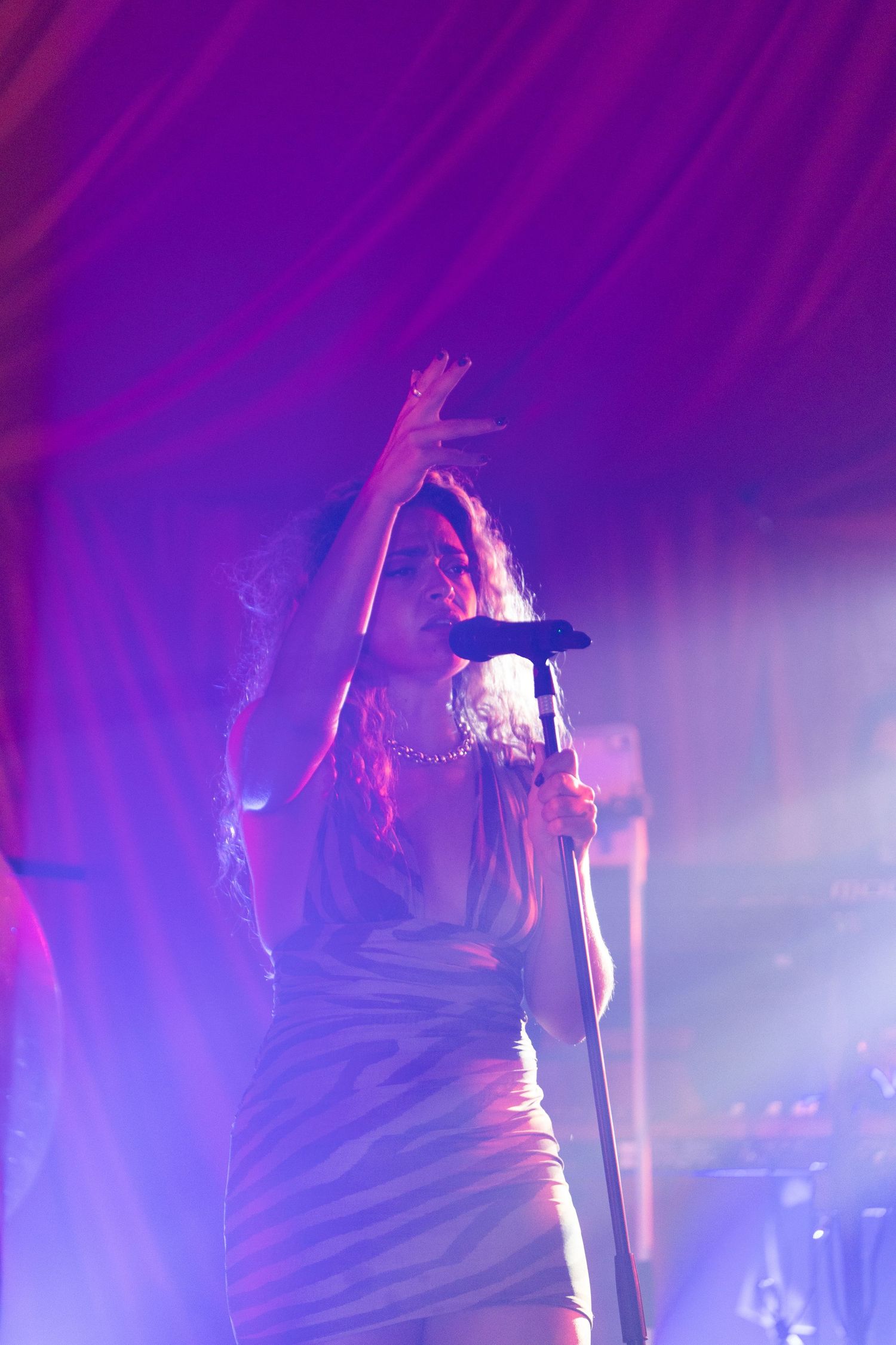 Silhouetted performer singing on stage with dramatic purple and blue lighting effects in the background.
