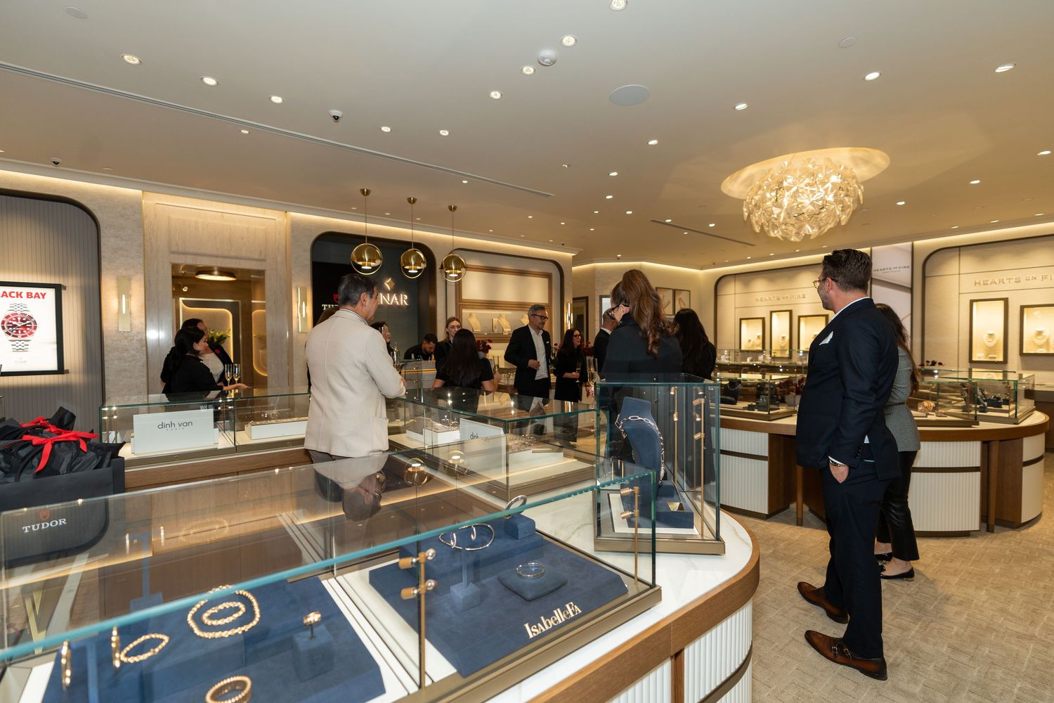 Customers browse luxury jewelry displays in an upscale retail store with bright lighting and glass showcases.