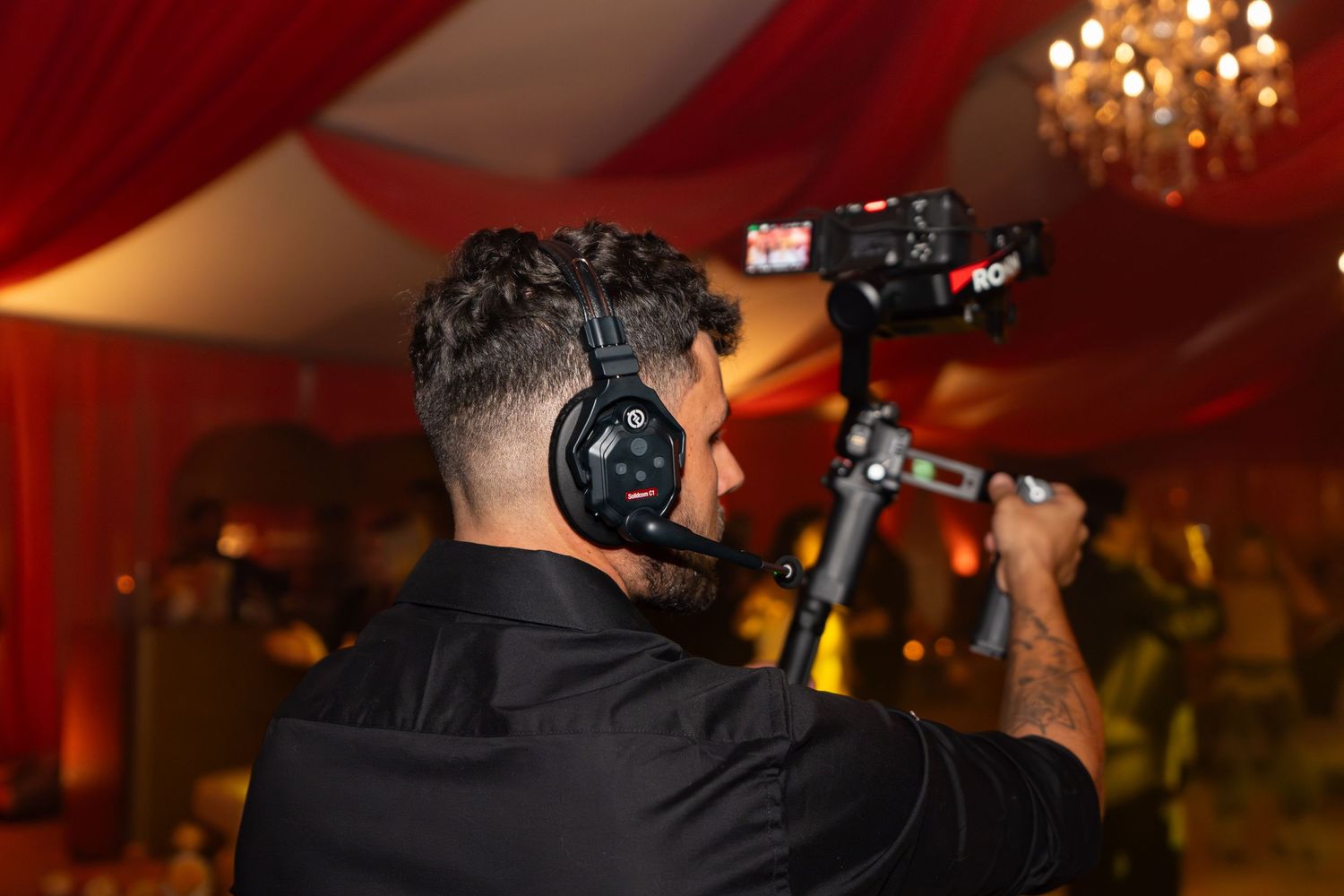 DJ wearing headphones performs at an elegant event with warm lighting and chandeliers in the background.