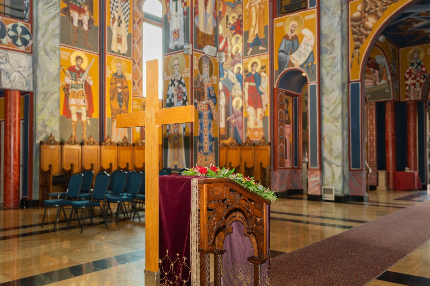 Interior of ornate Orthodox church with colorful religious frescoes, marble columns and wooden lectern in Belgrade, Serbia.