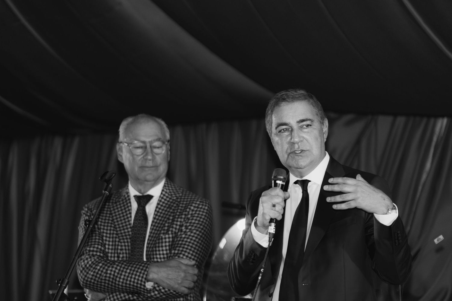 Black and white photo collage showing multiple men in suits sitting and speaking at what appears to be a panel discussion.