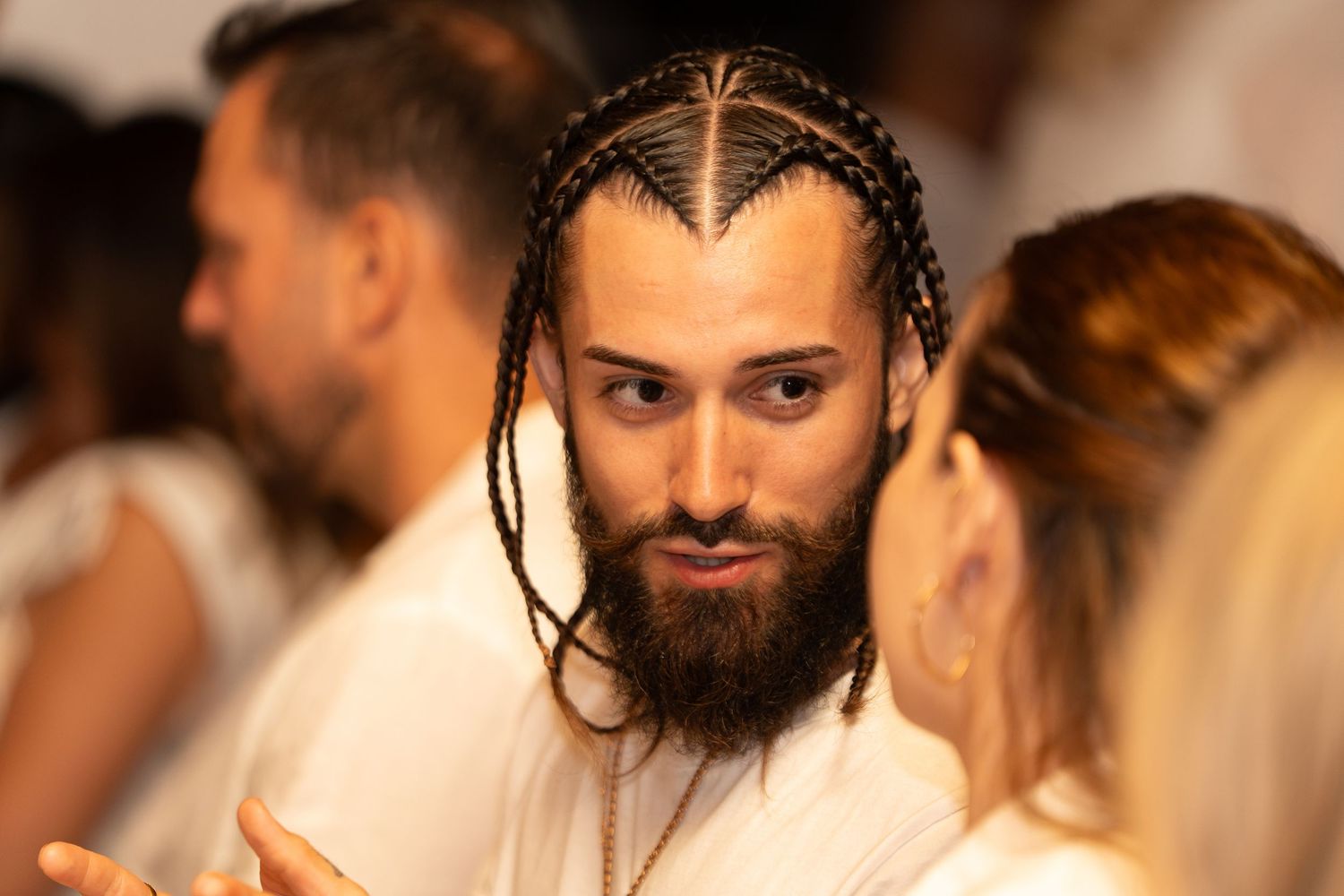 Person with braided hair and beard engaged in conversation at a social gathering.