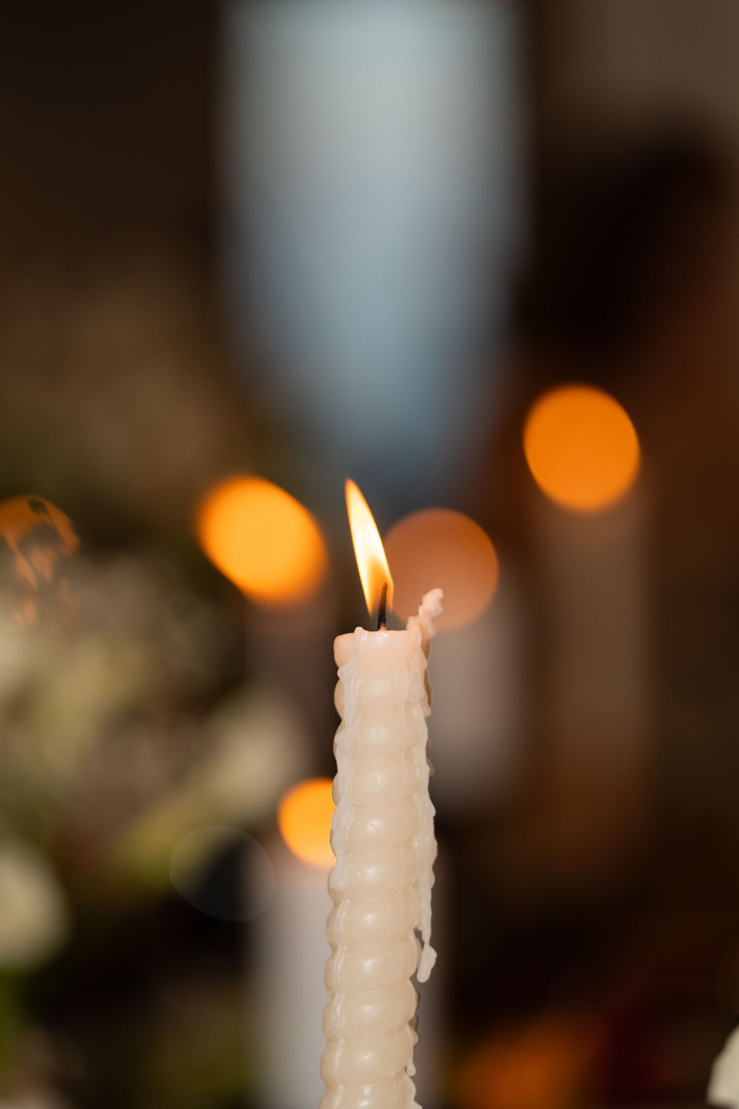 Three lit white taper candles against a dark background with glowing bokeh lights create an elegant atmosphere.