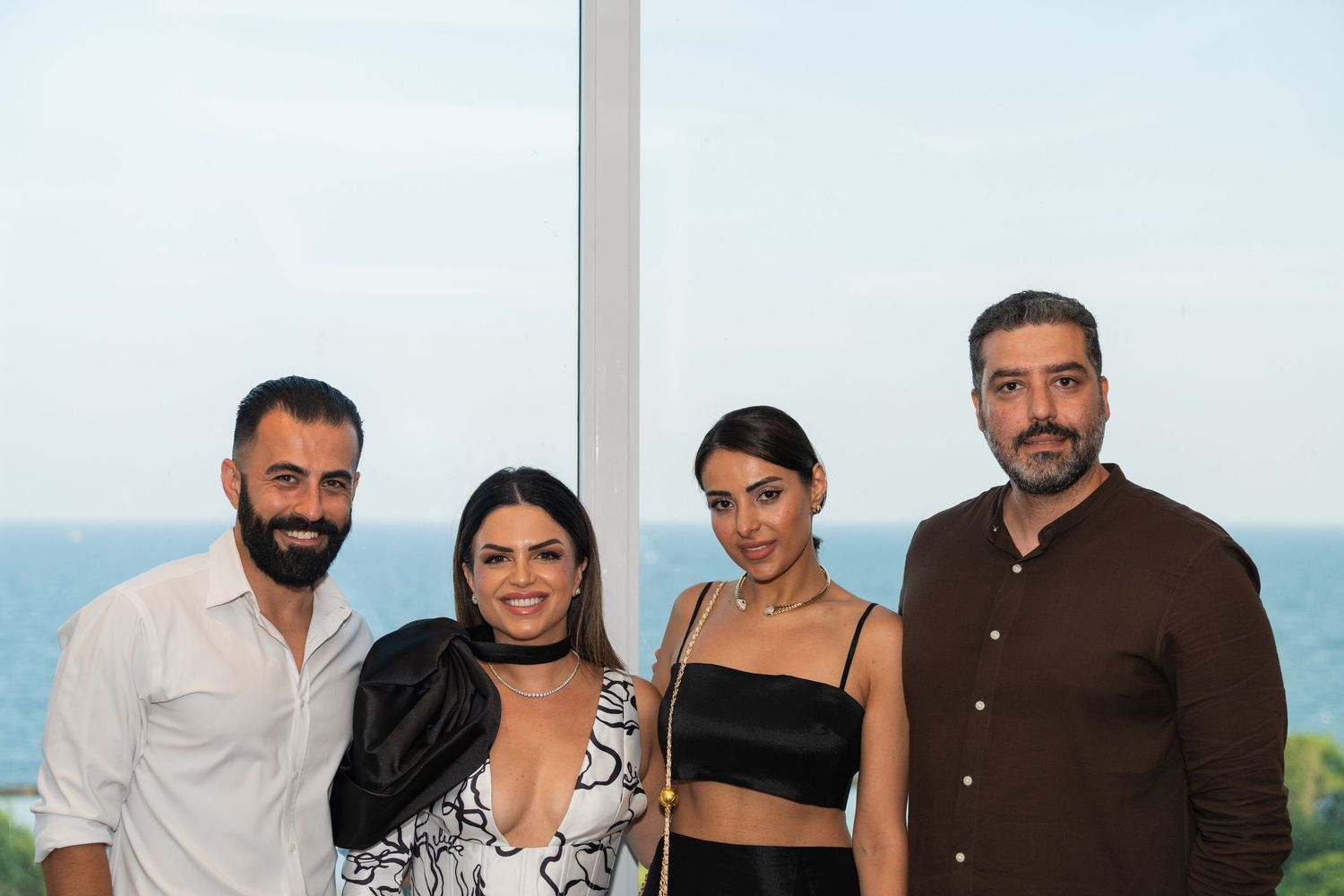 A small group stands together outdoors smiling with water and landscape views visible in the background.