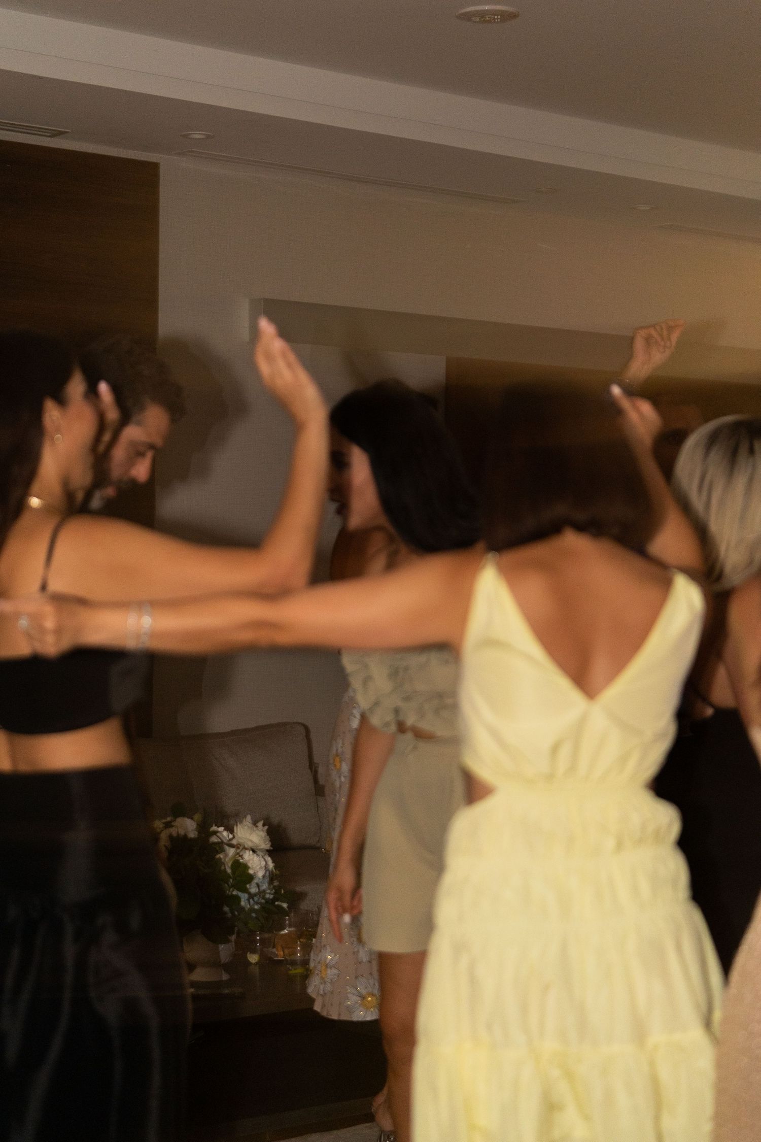 A group dances in a line with arms outstretched, one person wearing a yellow dress in the foreground.