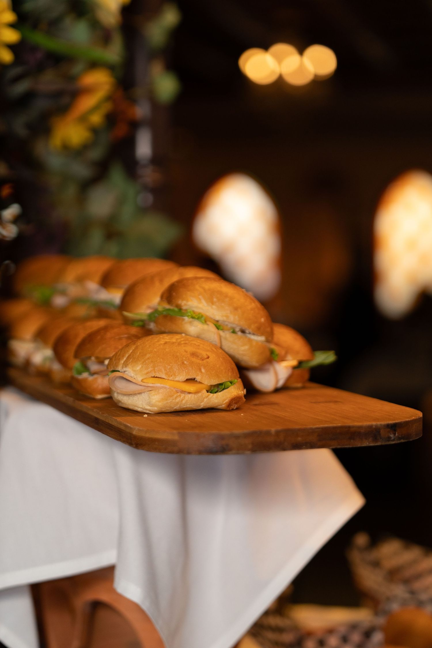 Fresh sandwich sliders arranged on a wooden serving board with a white tablecloth.