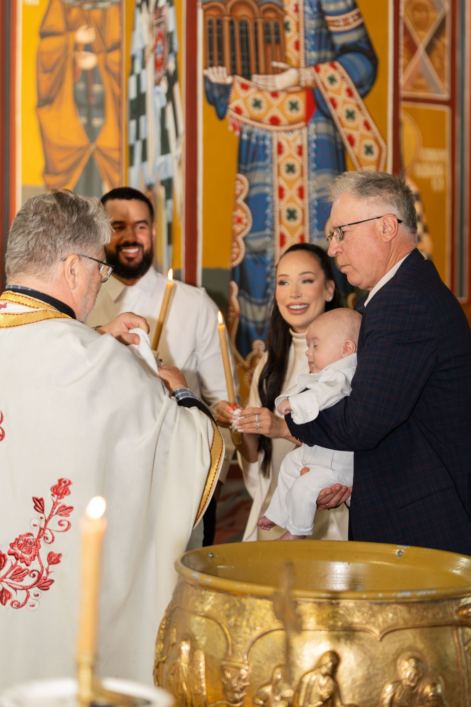 A group of people in white ceremonial robes gather around golden baptismal fonts during a religious ceremony.