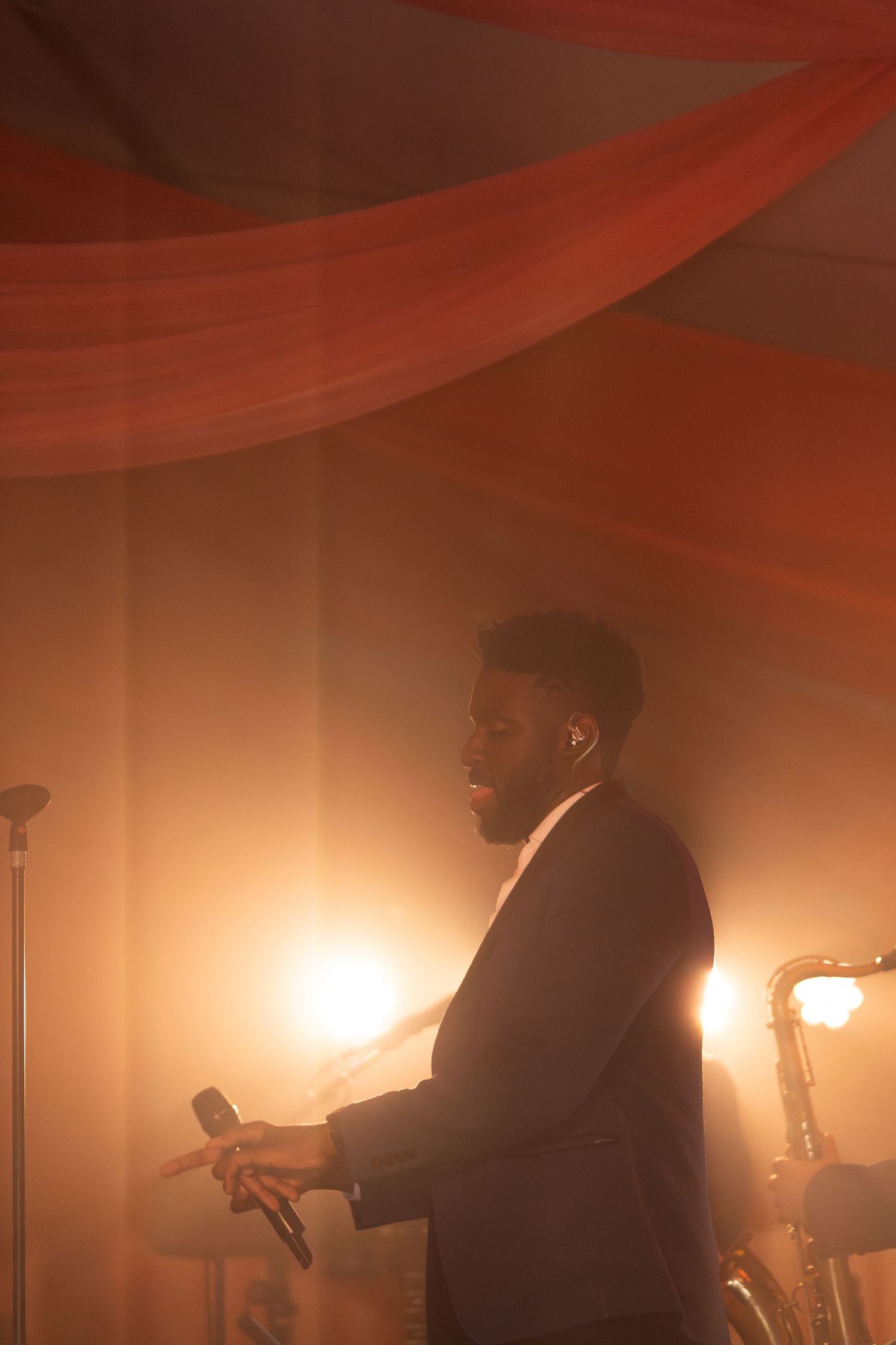 Musicians perform in dramatic red lighting creating silhouettes against a warm atmospheric background.