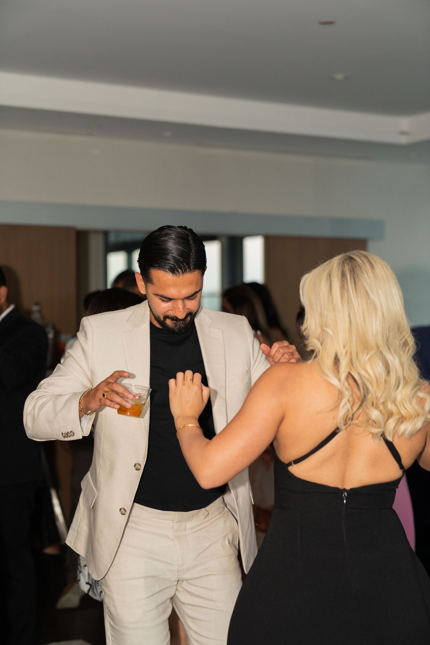 A couple dancing together at an event wearing formal attire, with the woman in a black dress and man in light colored suit.