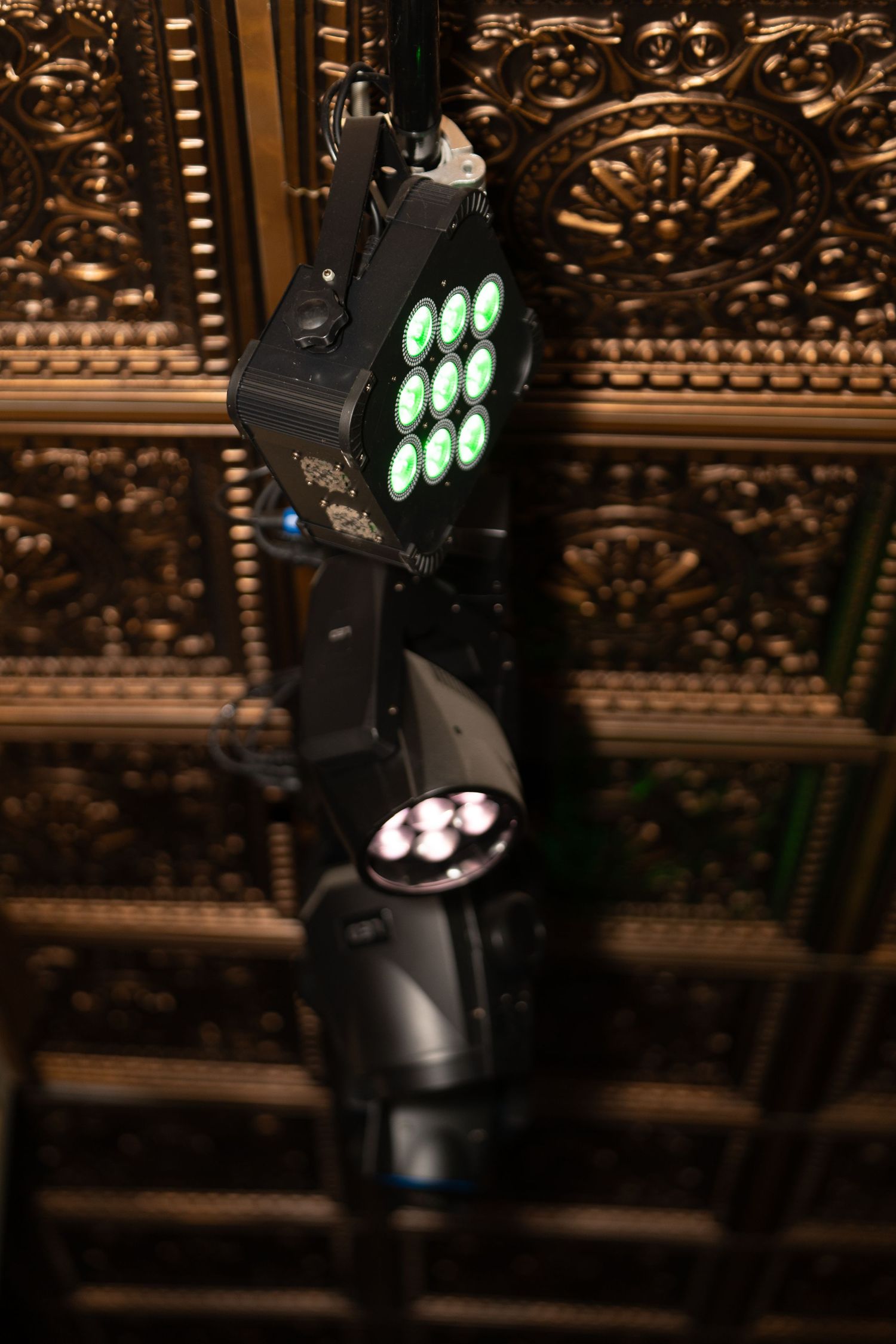 Professional stage lighting equipment with green LED lights mounted against an ornate ceiling.