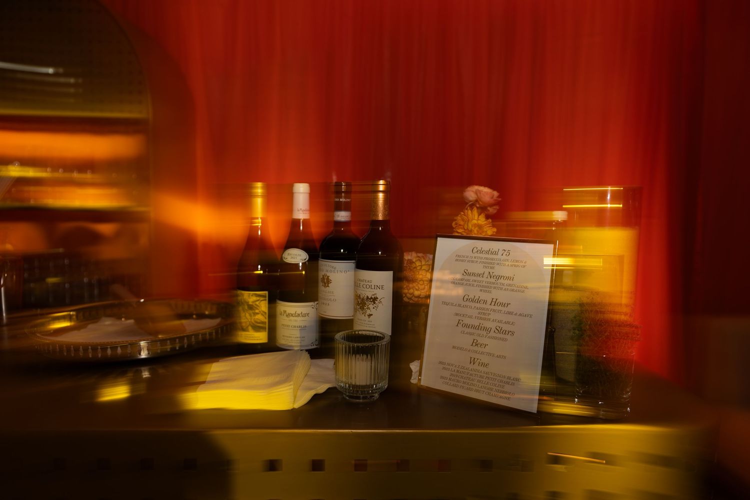 A dimly lit bar interior with red ambient lighting and bottles of liquor on display creates an intimate atmosphere.