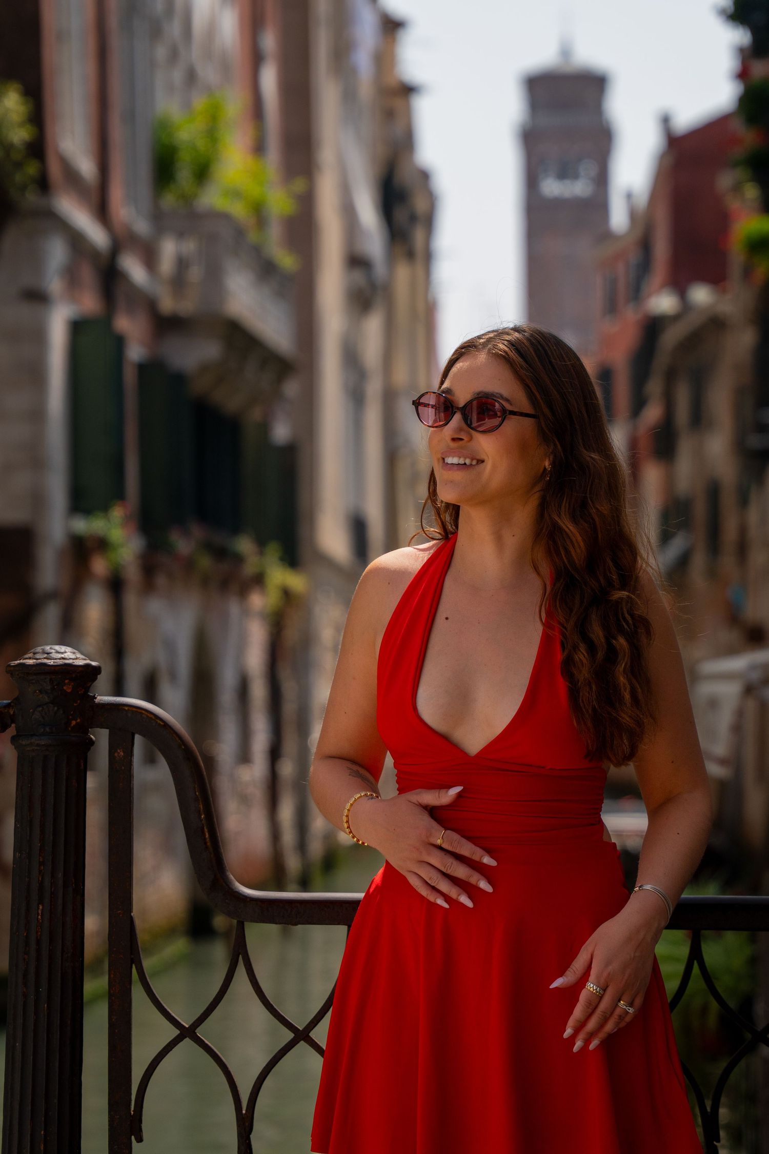 A woman in a red dress laughs while posing against a Venetian canal backdrop.