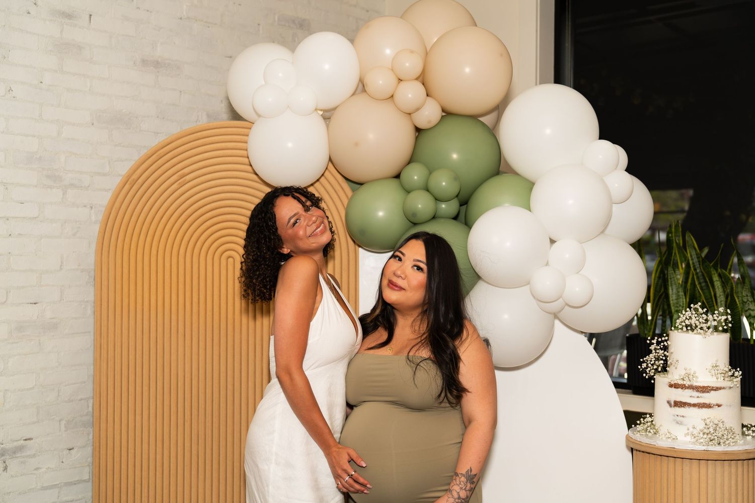 Elegant party setup with white and beige balloon arch decorations against a white brick wall.