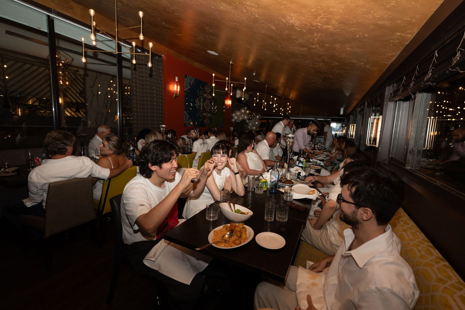 Diners enjoying a meal at a dimly lit restaurant with ambient lighting and wood tables.
