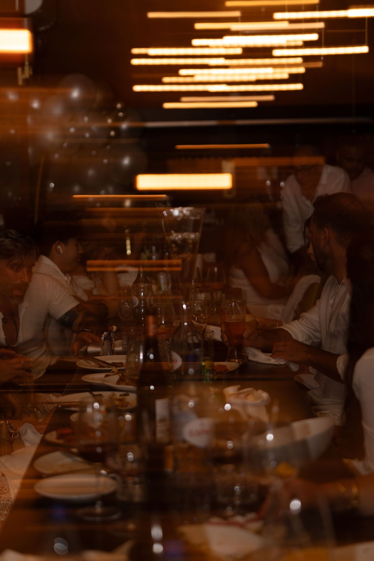 Moody restaurant scene with glowing light fixtures and diners seated at tables in soft focus.