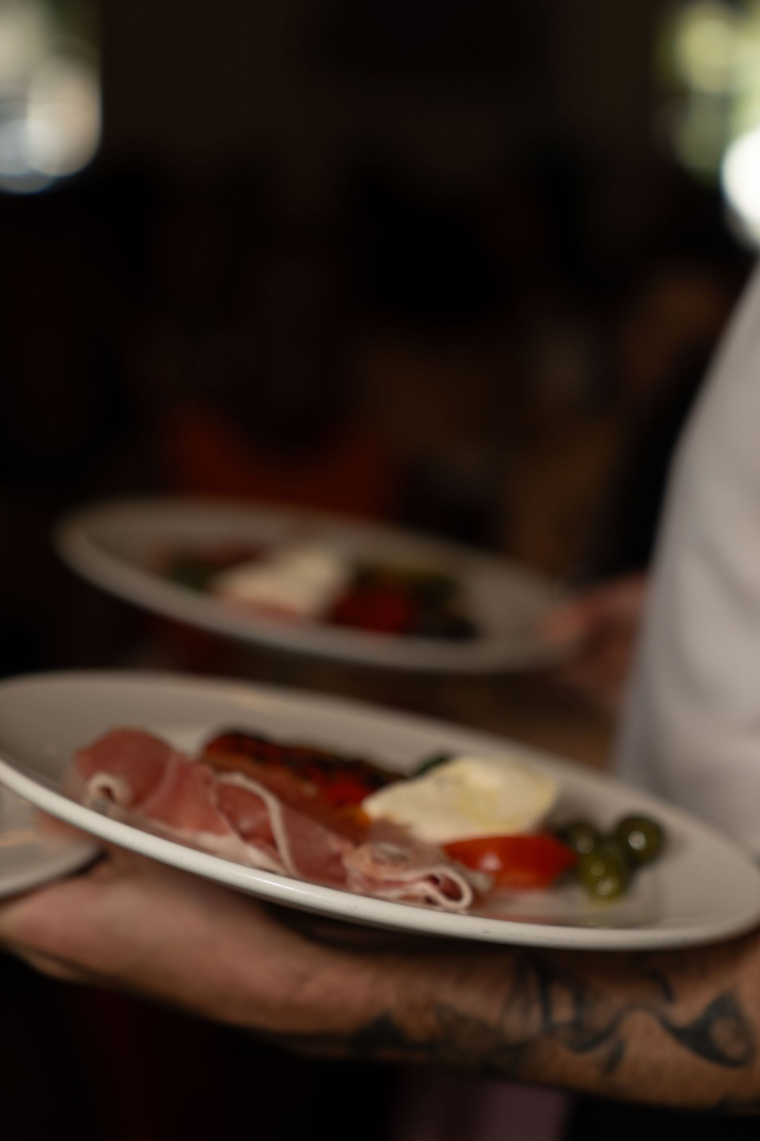 Charcuterie board with sliced meats and garnishes served on white plates at a restaurant.