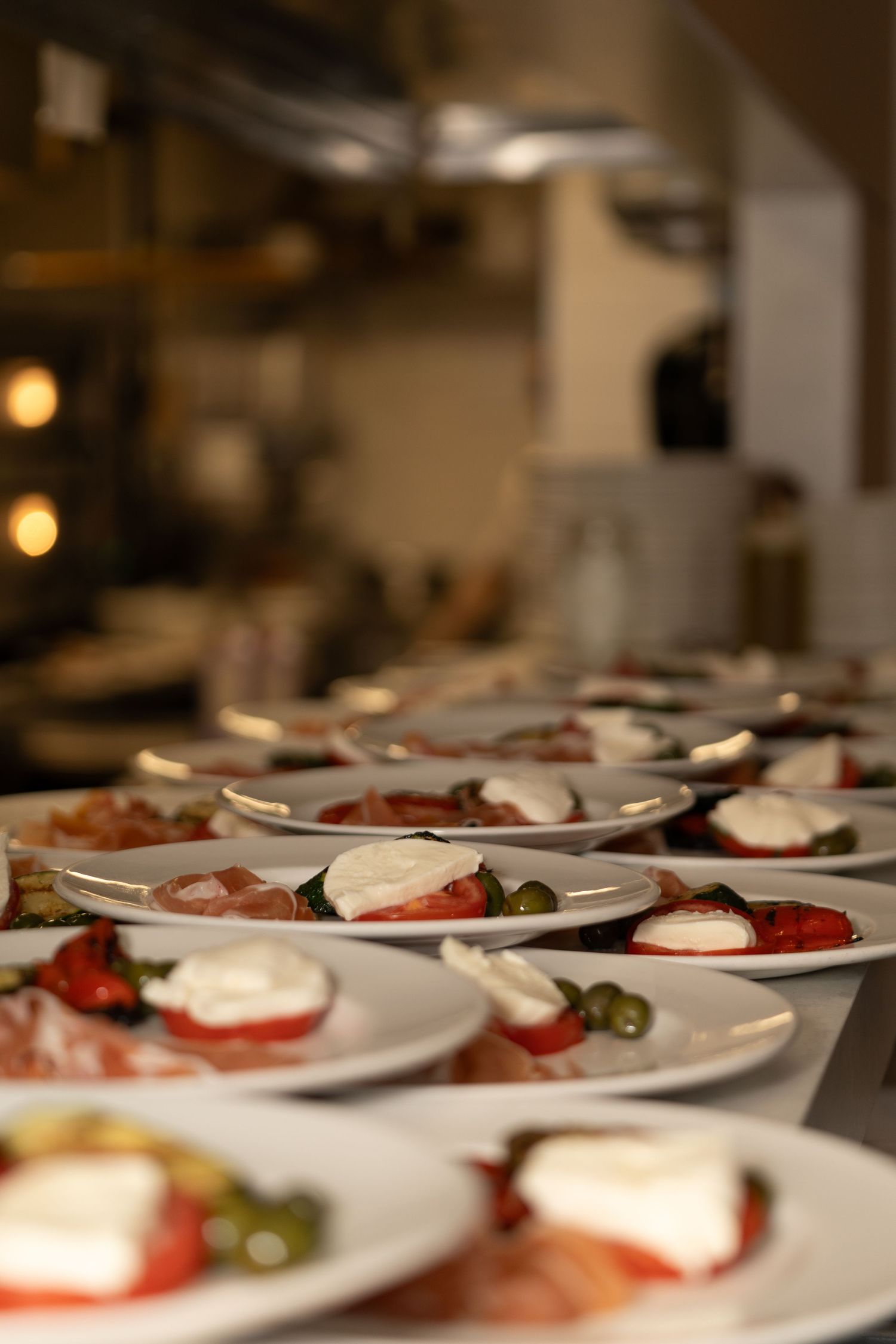 Row of elegant caprese salad plates with mozzarella and tomatoes in a restaurant kitchen.