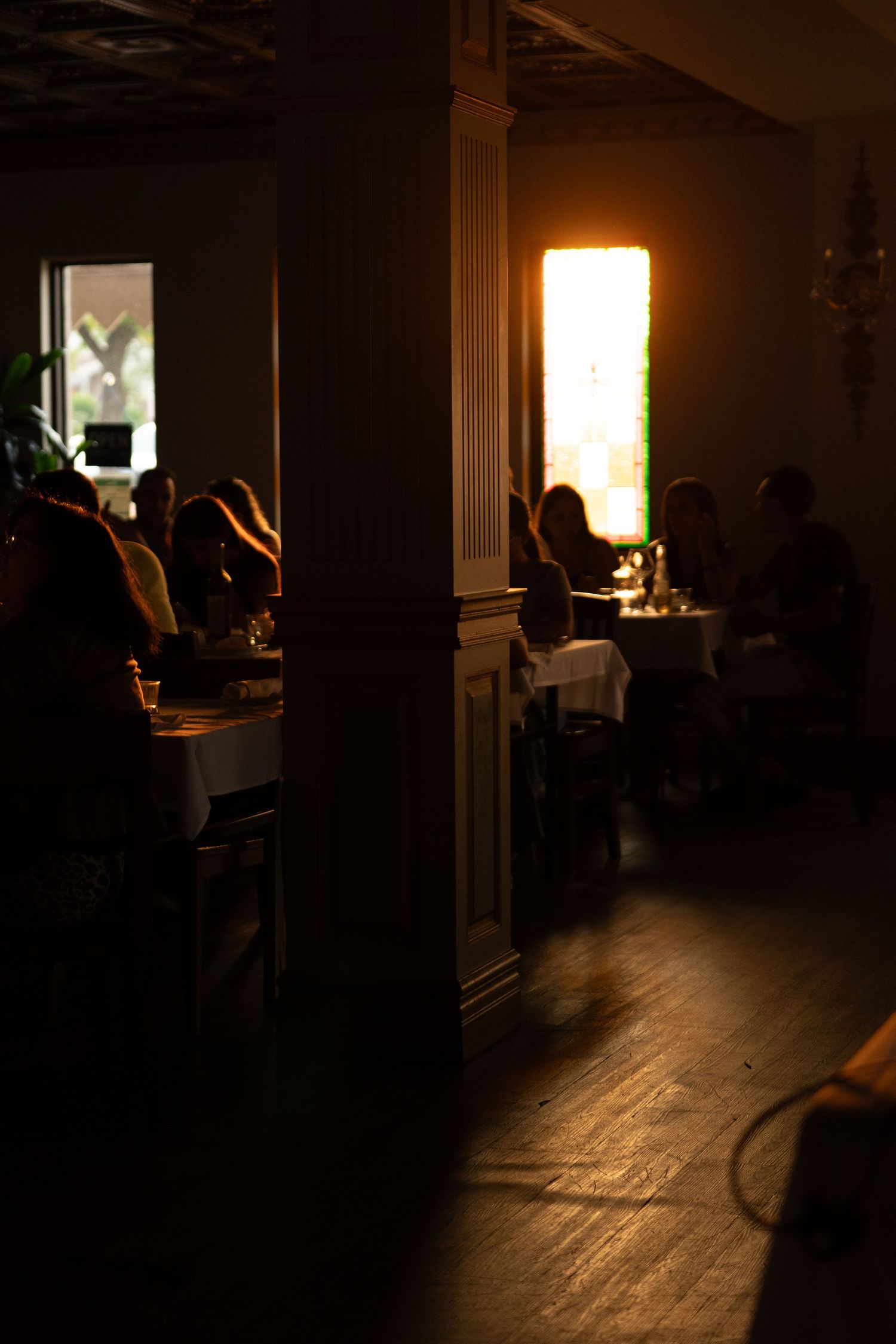 A dimly lit restaurant interior with tables and silhouettes of diners creating an intimate ambiance.