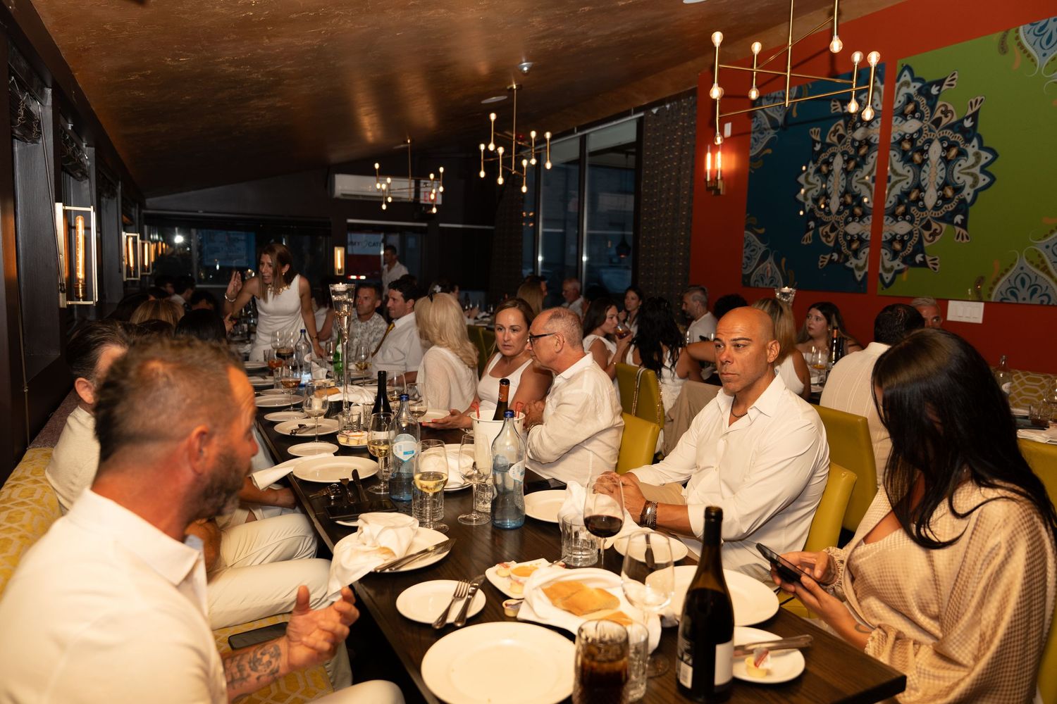 Large group dining together at a long restaurant table with wine and plates.