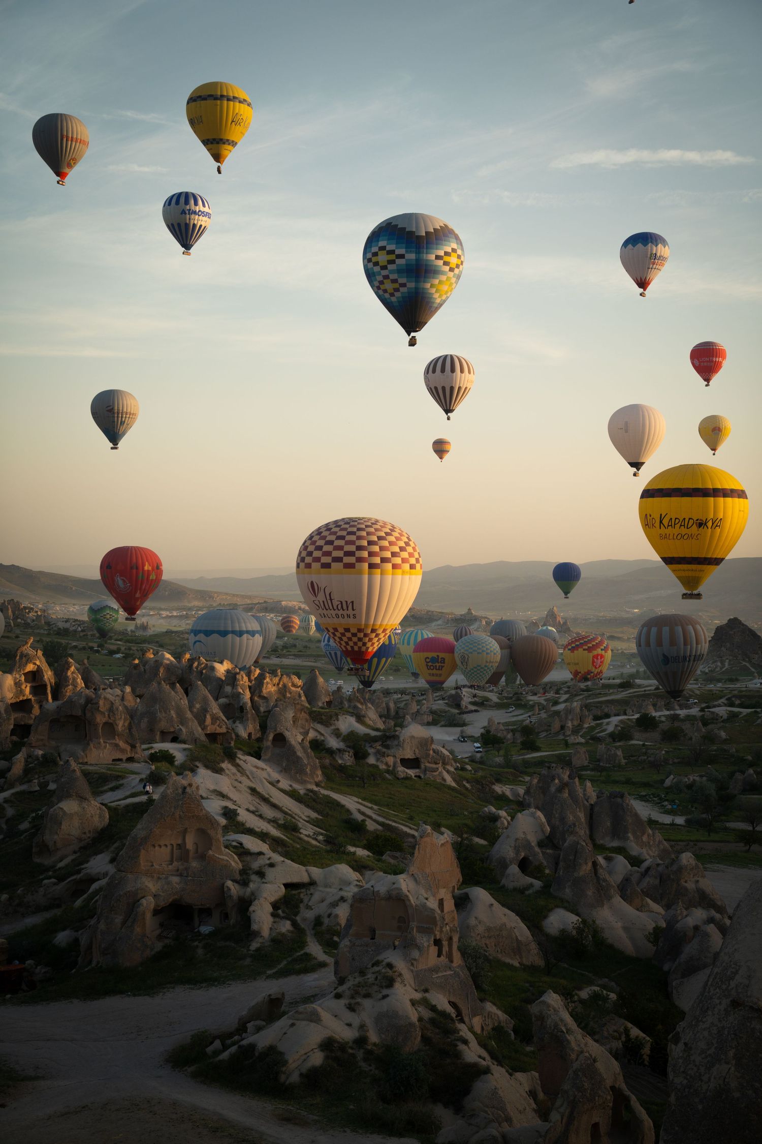 Colorful hot air balloons floating over rocky landscape of Cappadocia during sunrise.