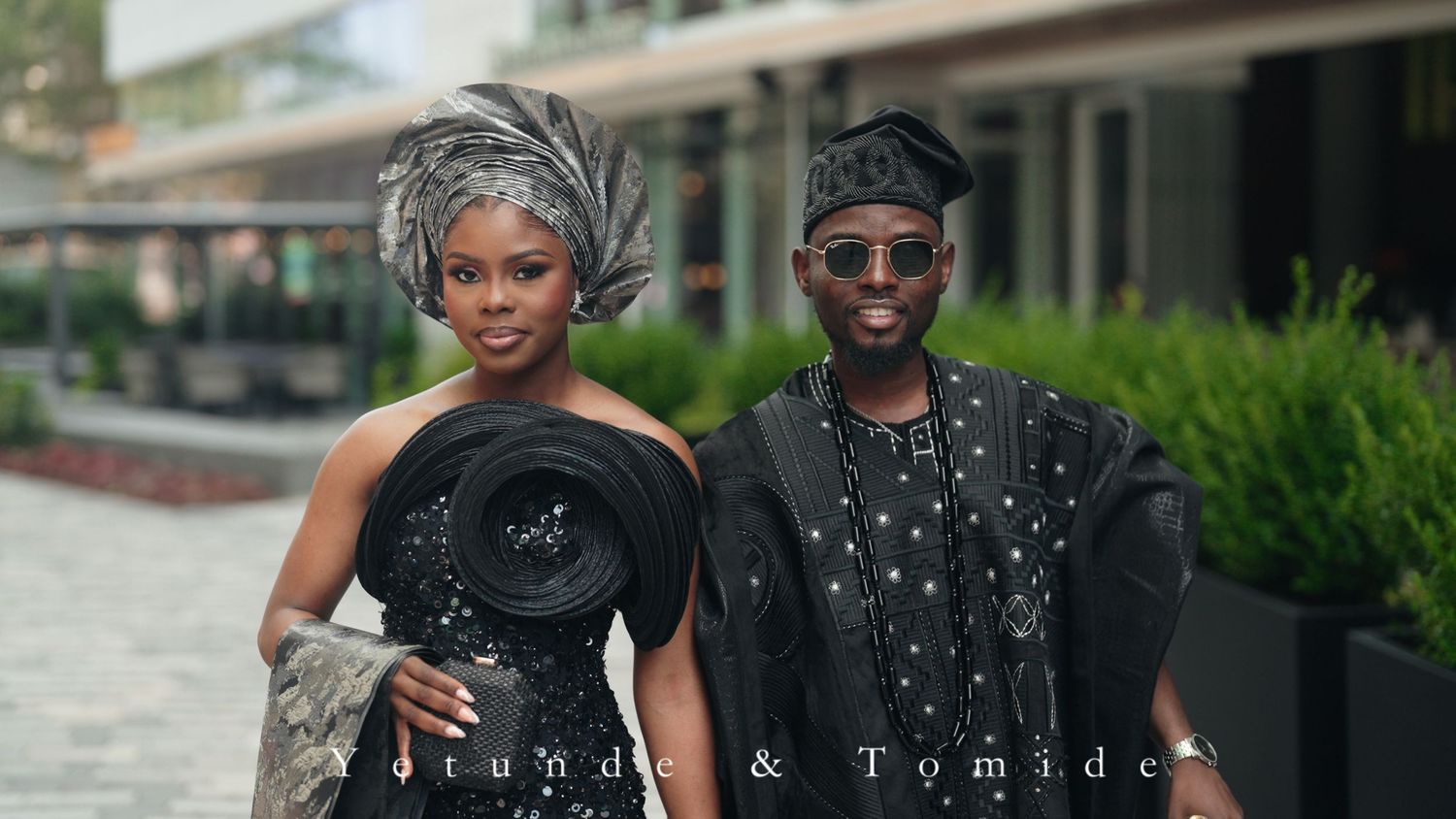 Elegant Nigerian couple in traditional black attire pose together outdoors for their wedding photo.