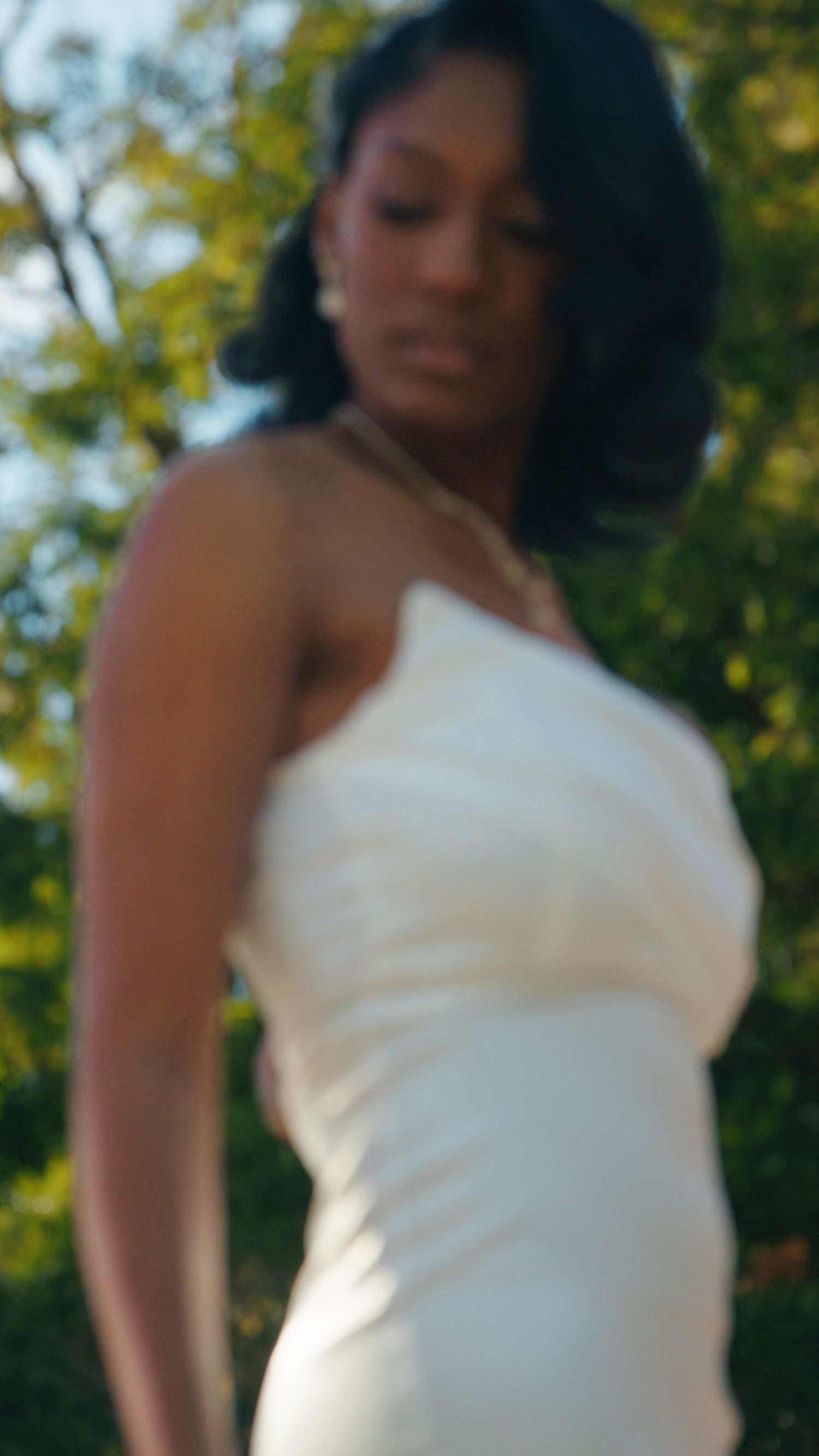 Elegant bride in a white strapless gown posing outdoors with lush green trees in the background.