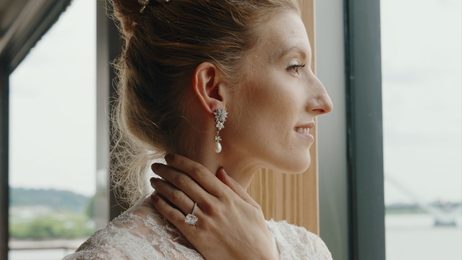 Beautiful bride in profile wearing elegant diamond drop earrings and engagement ring by window.