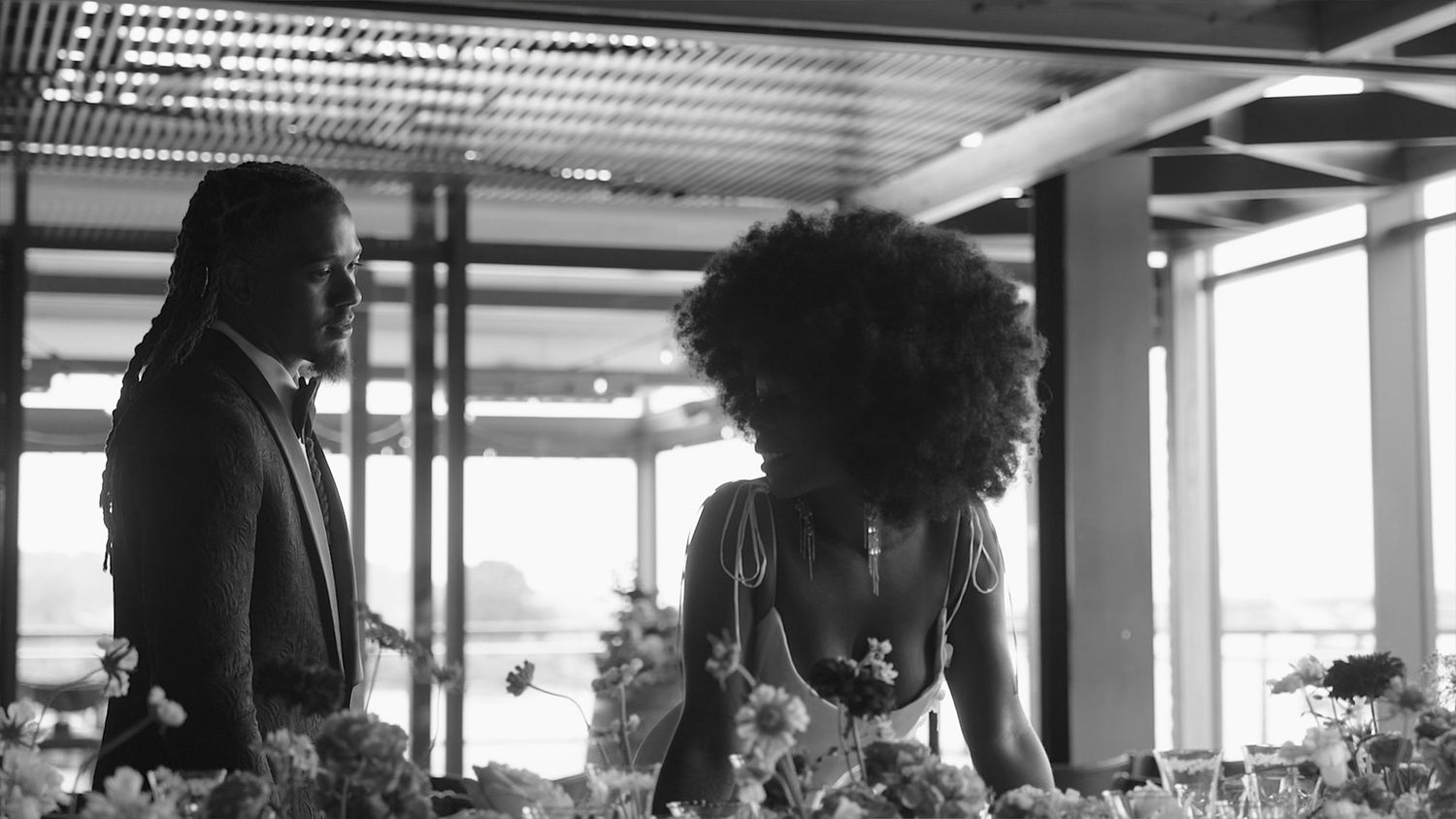 Black and white photo of couple sharing intimate moment surrounded by floral arrangements.