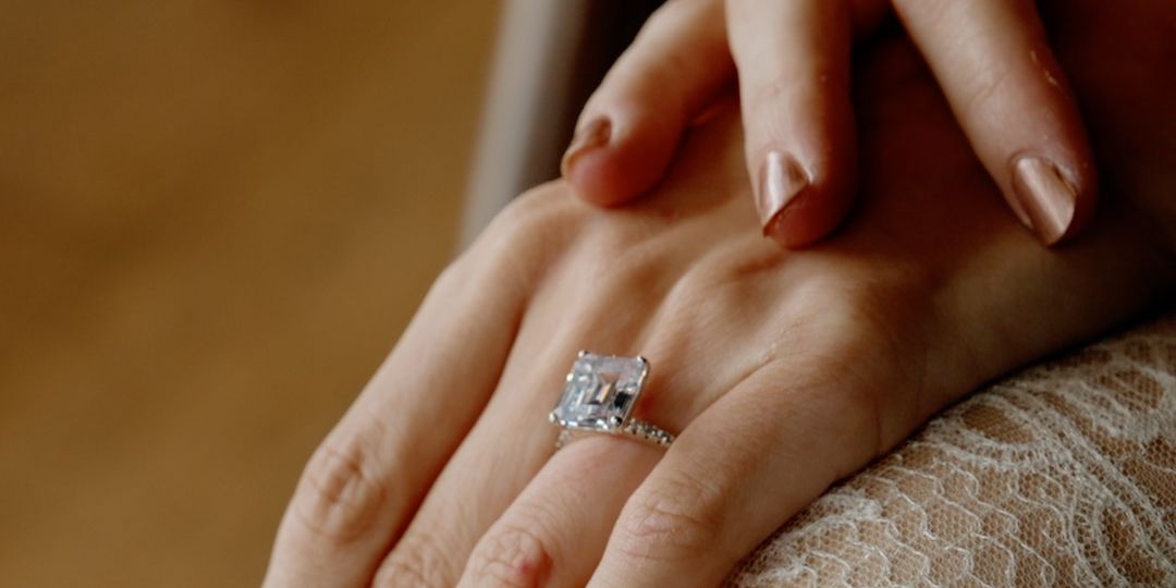 Close-up of stunning emerald-cut diamond solitaire engagement ring on bride's hand.