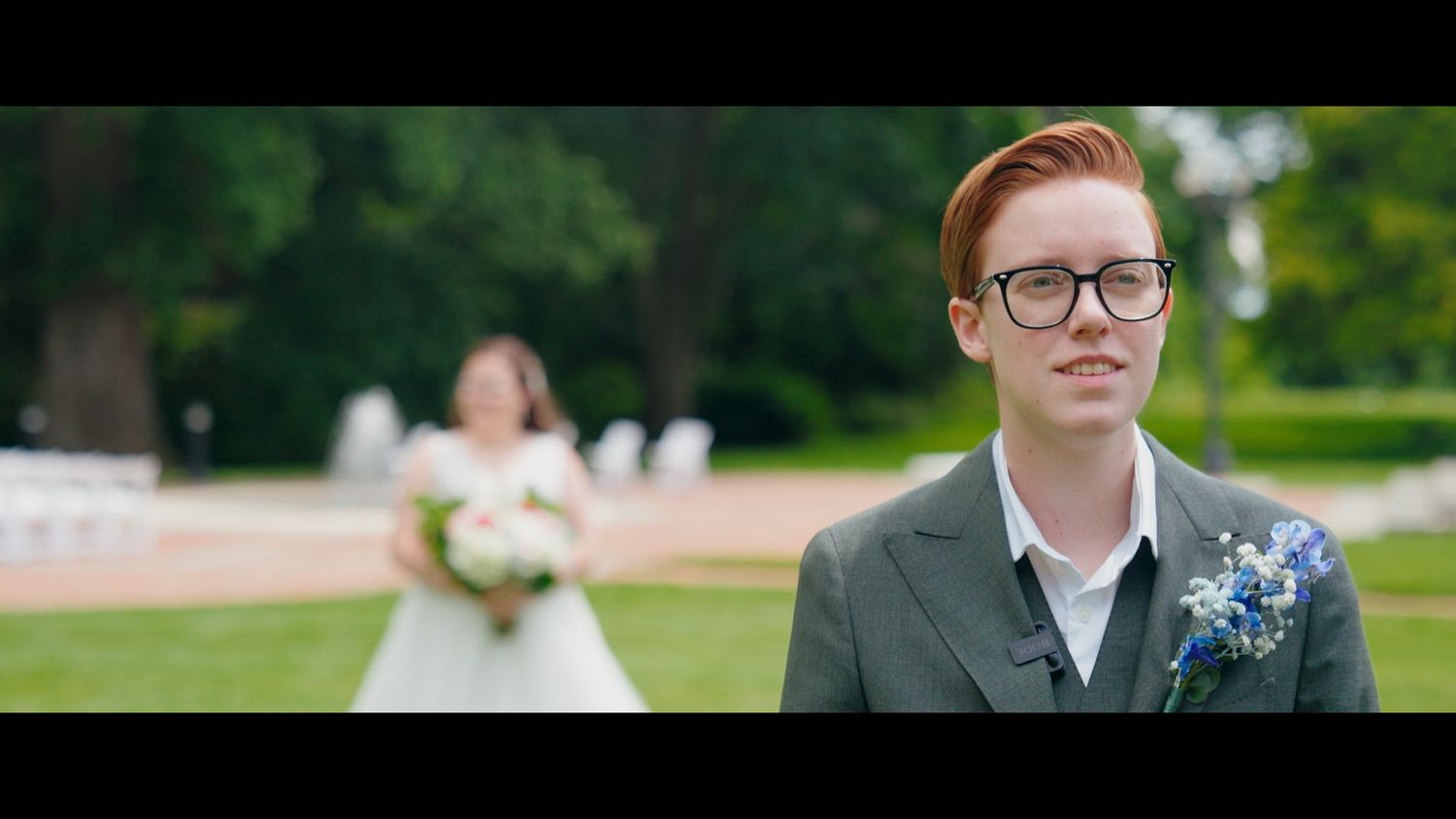 Red-haired groom in gray suit wearing glasses emotional during first look with bride approaching outdoors.